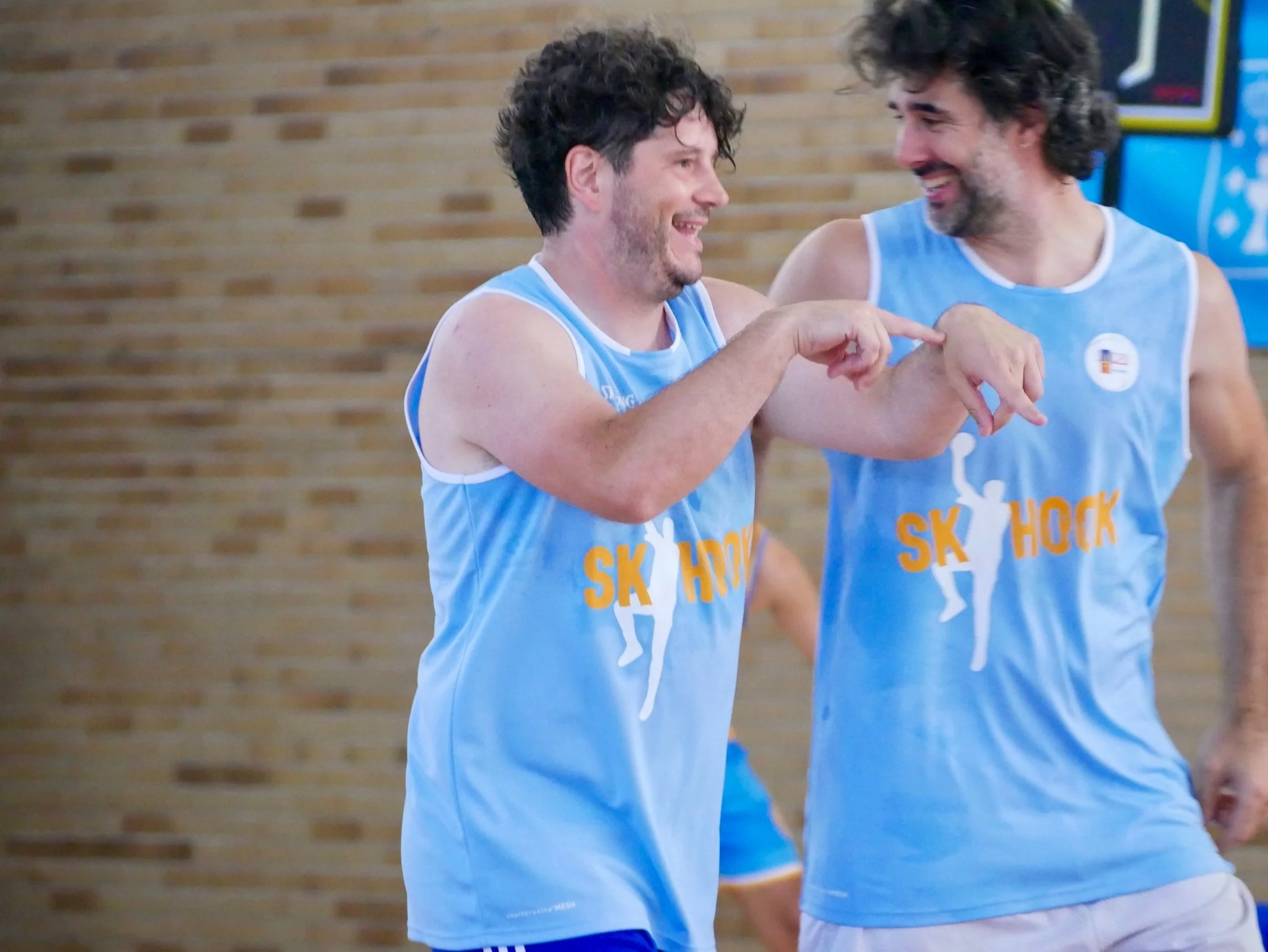 Dos jugadores de baloncesto con uniformes azules que dicen SK SHOCK, sonriendo y celebrando en una cancha.