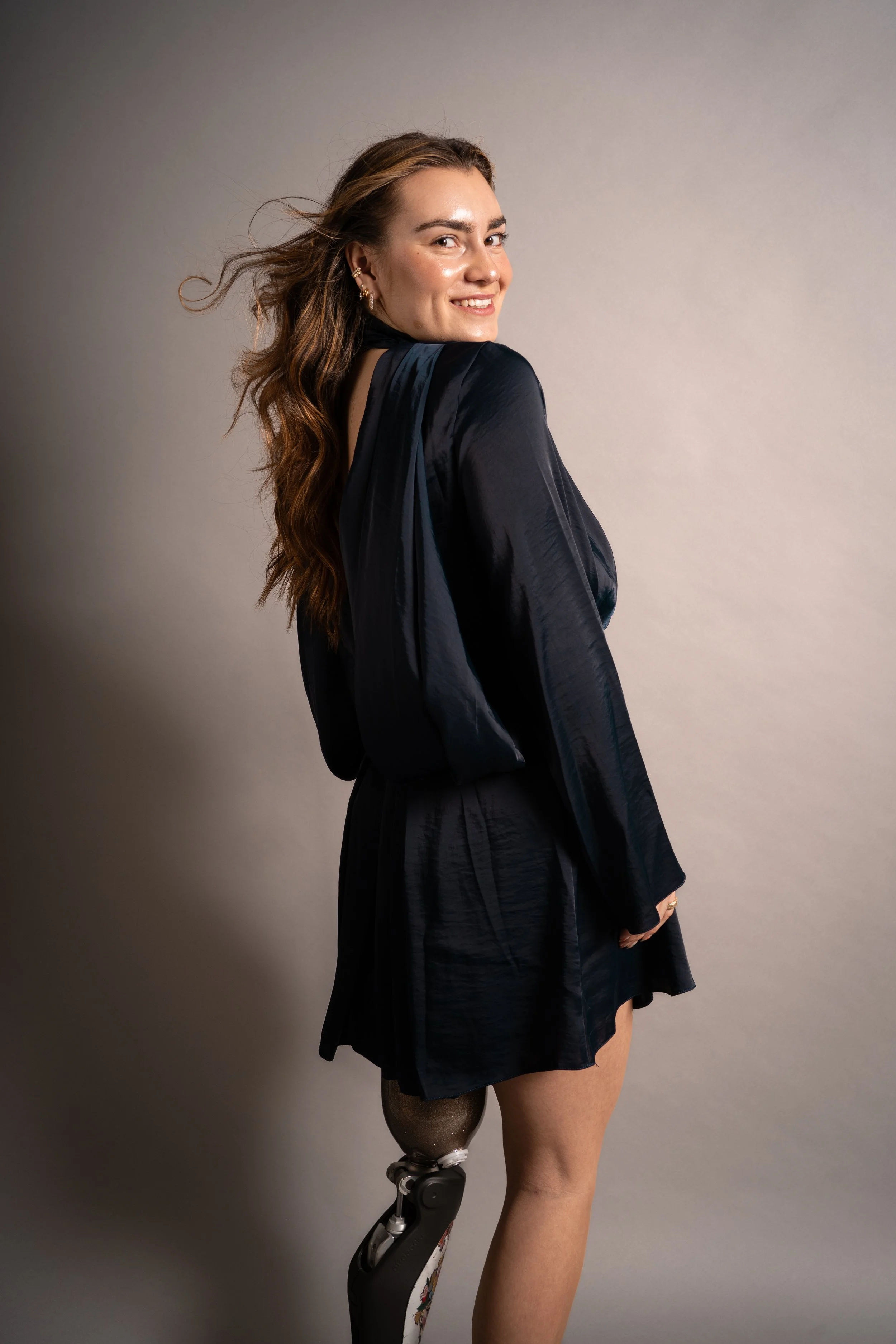 Junge Frau mit langem braunen Haar, lächelnd, trägt dunkle Kleidung, hat einen künstlichen Unterkörper und ein Beinprothese.