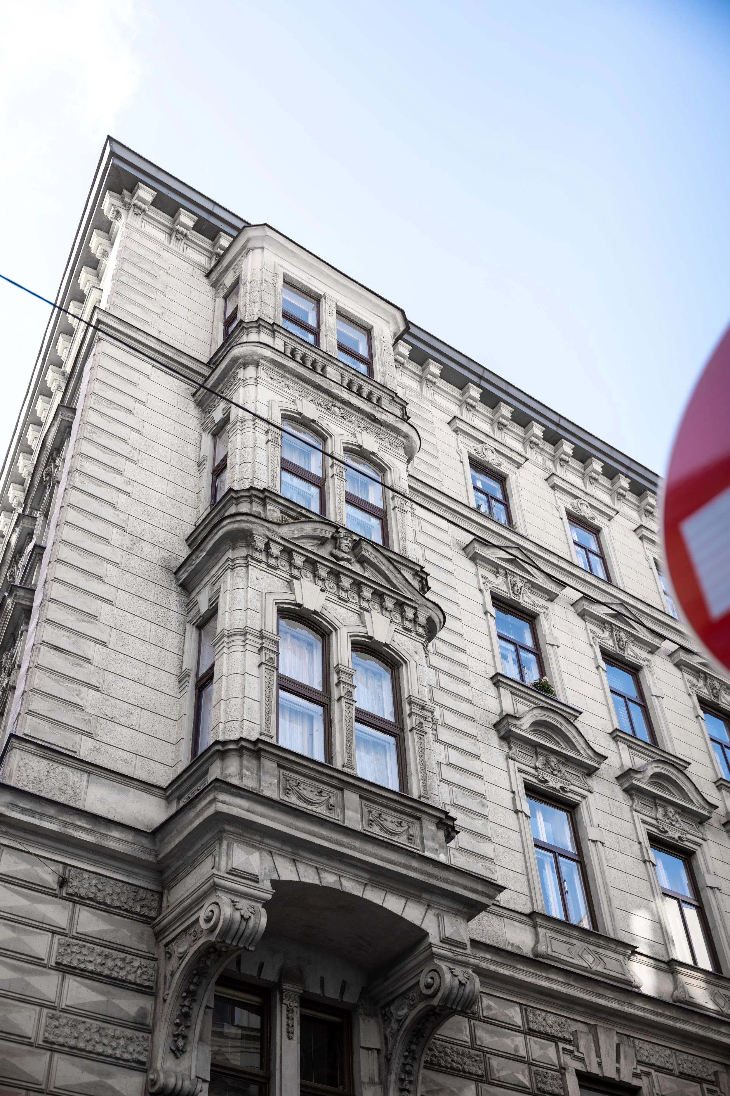 Historische mehrstöckige Gebäude mit Ornamenten und großen Fenstern, Blick nach oben, blauer Himmel, teilweise sichtbares Verkehrszeichen.