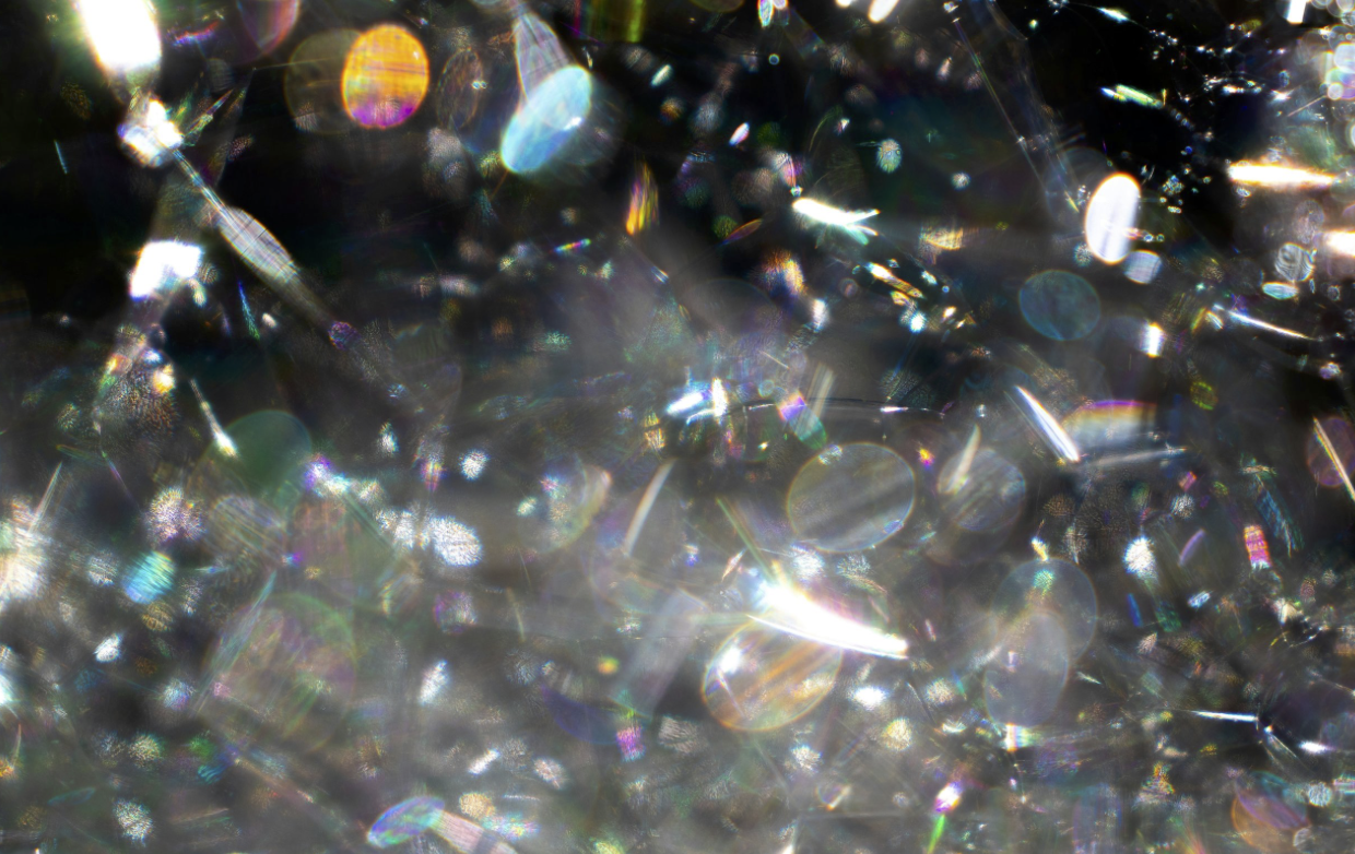 Close-up of reflective, sparkly, and iridescent crystals or beads creating a shimmering, colorful surface.