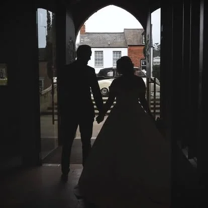 Silhouettes of a man and woman holding hands, standing in a doorway, with houses and a car outside