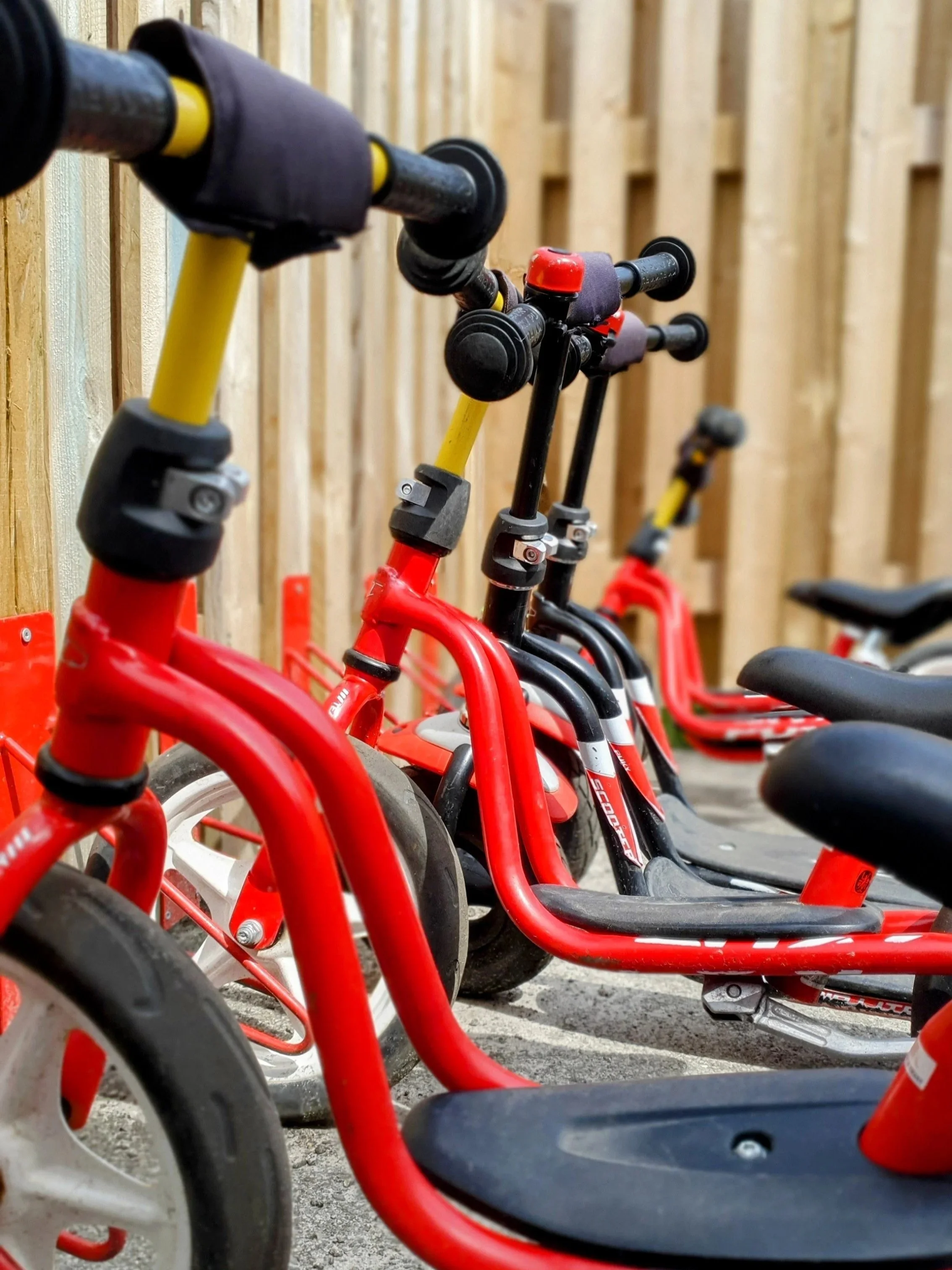 Rød børnecykel med sort sæde og styre, parkeret ved en træplade væg.