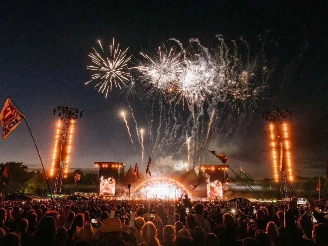 Festfyrværkeri over en stor festival med mange mennesker, scene og flag.