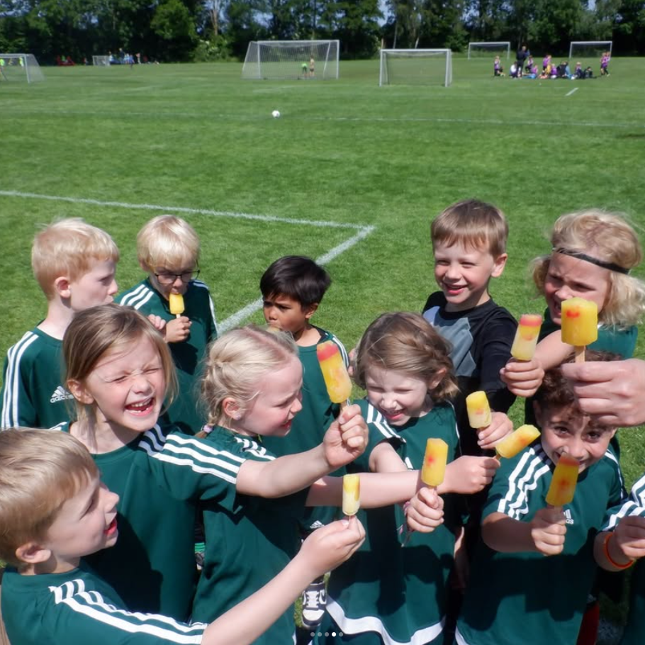 Et gruppebillde af glade børn i fodboldtøjer, der spiser is
