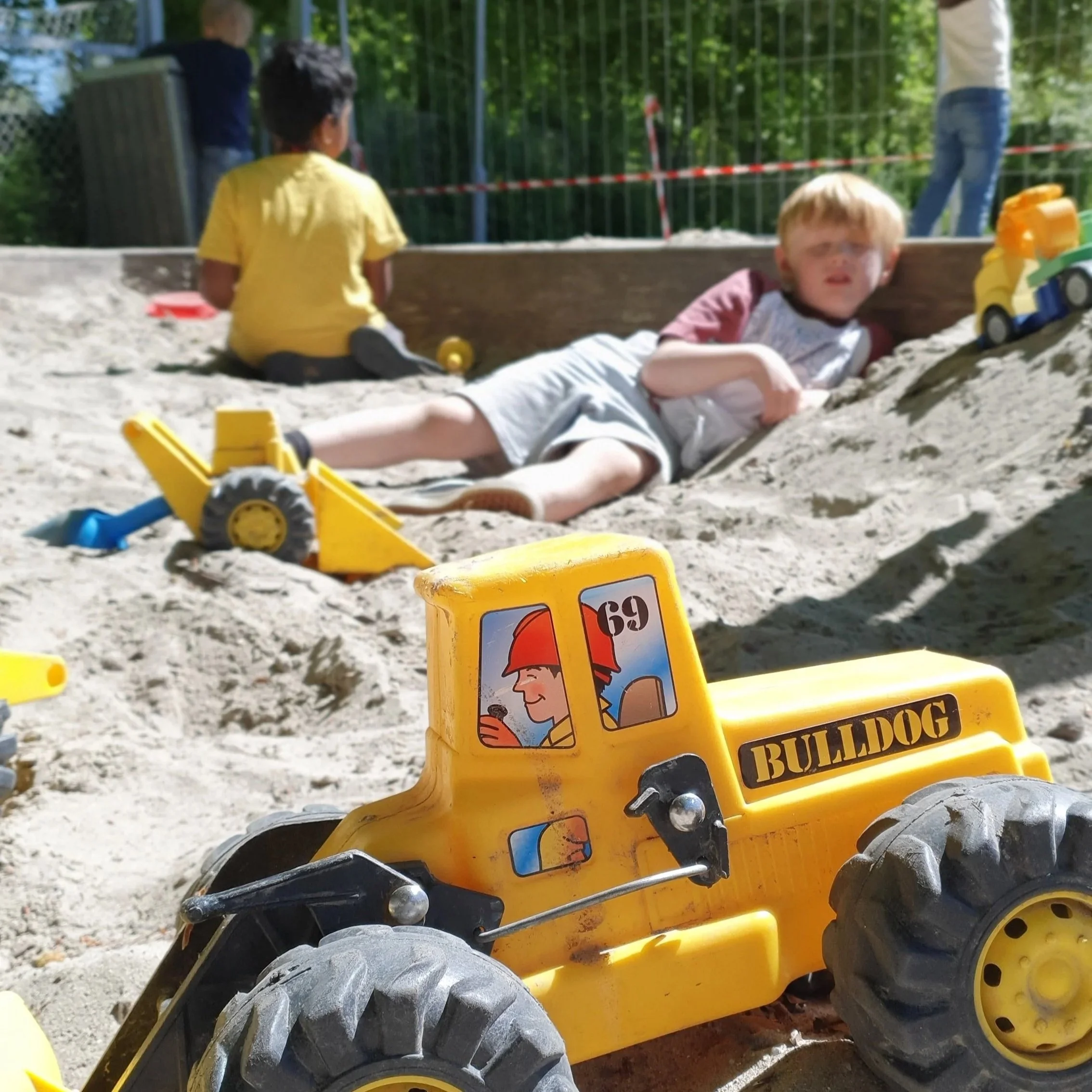 En dreng og  stor gul legetøjs buldozer i en sandkasse