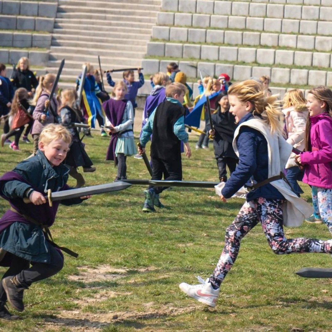 Børn der kæmper med plastiksværd i en kamp i en udendørs park.