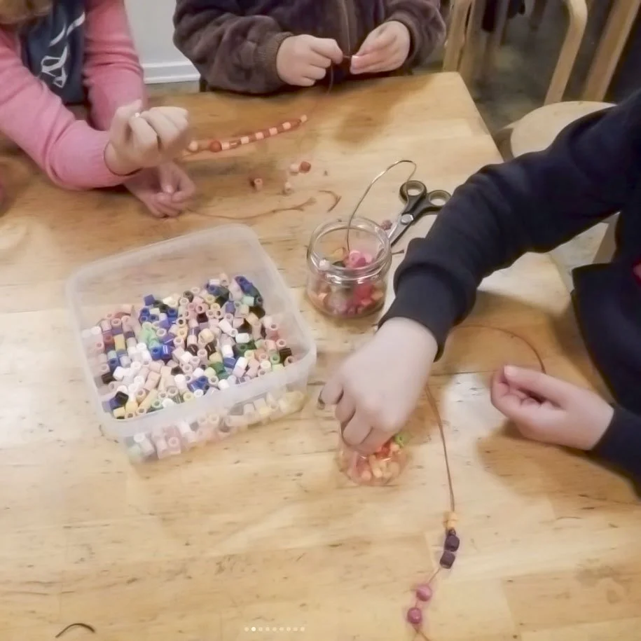 Børn arbejder med perler på et træbord, der har en gennemsigtig beholder og saks.