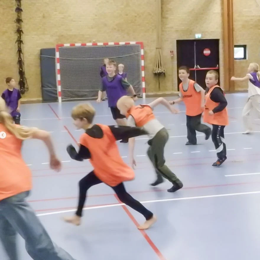 Børn leger fangeleg eller lignende spil i en gymnastiksal.