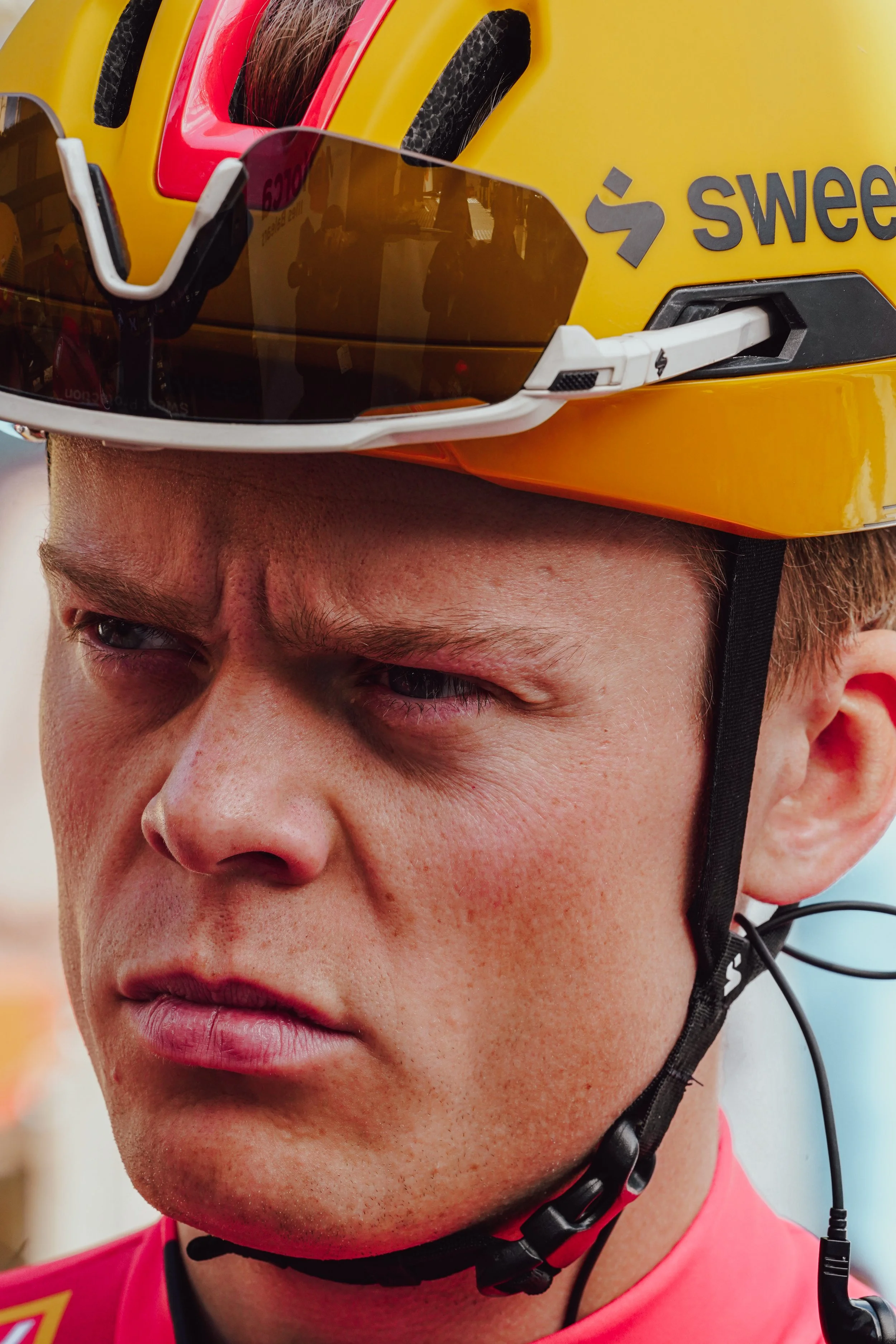 Close-up of a cyclist wearing a yellow helmet with sunglasses on top, showing a focused and serious facial expression.