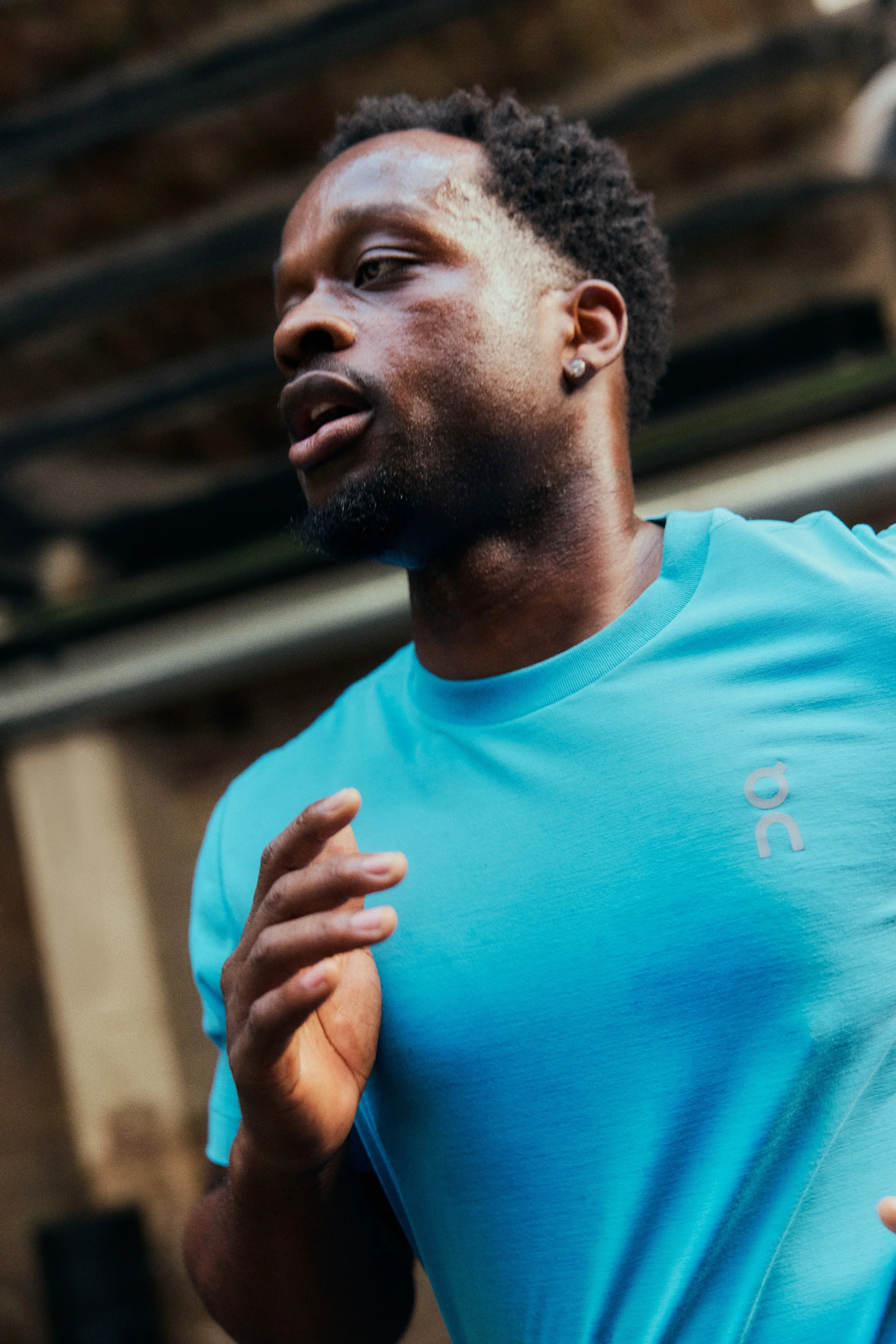 A man running and wearing a blue athletic shirt, with a serious expression, in an indoor or gym setting.