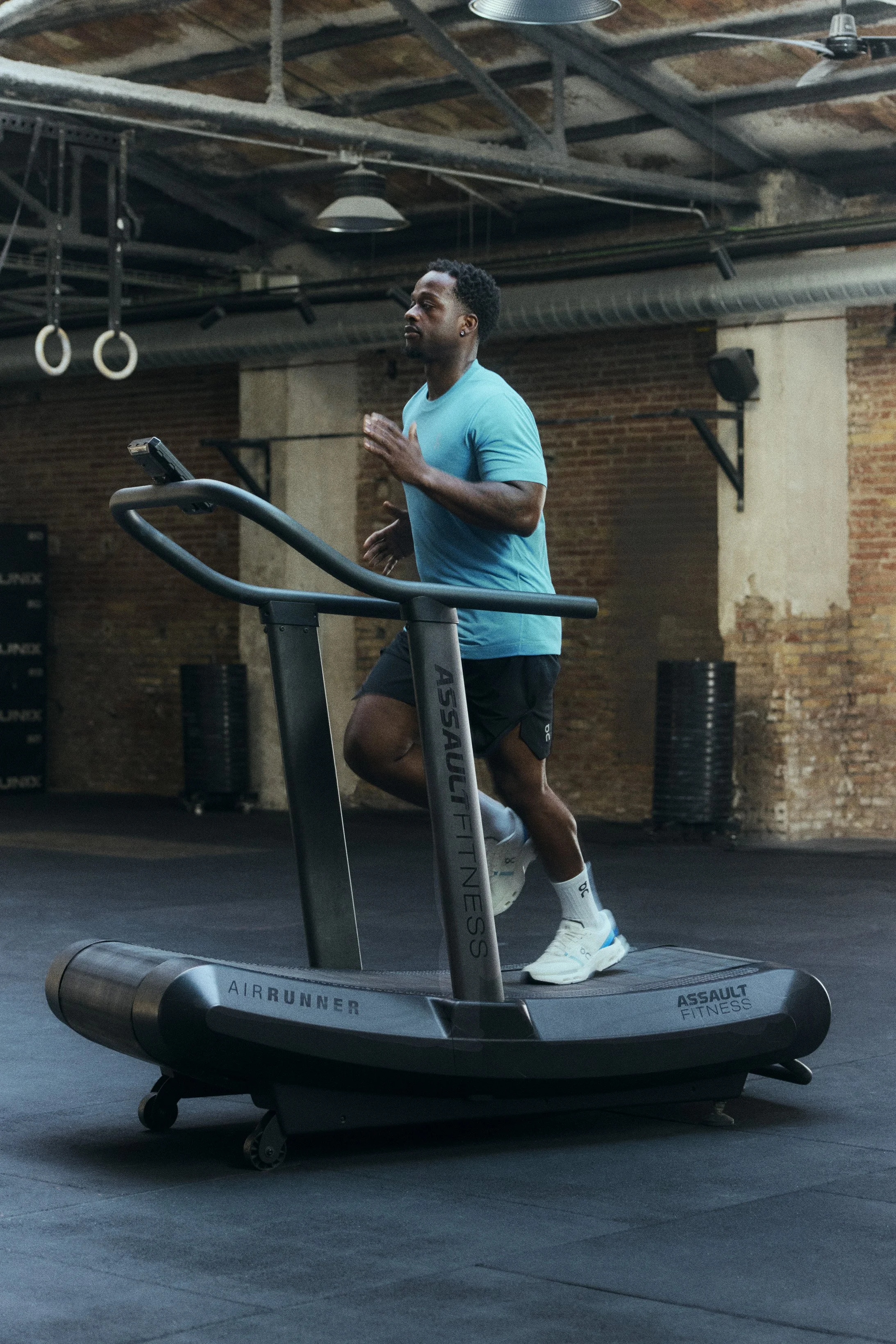 A man running on a treadmill inside a gym with exposed brick walls.