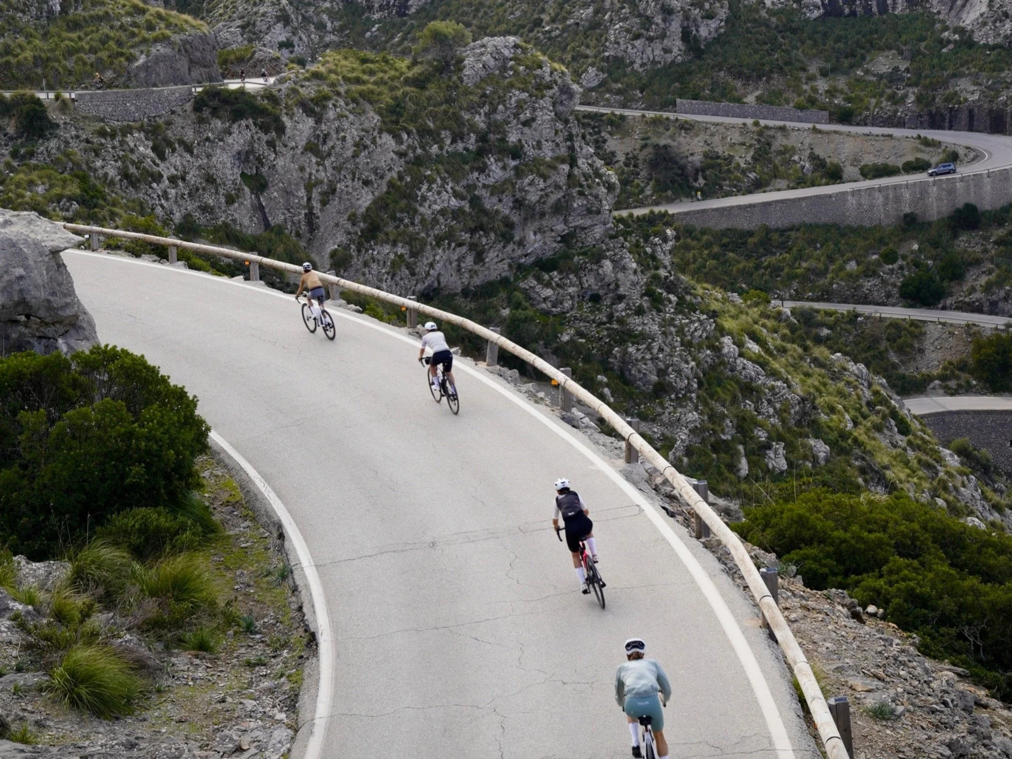Four cyclists riding uphill on a winding mountain road with a rocky and green landscape.