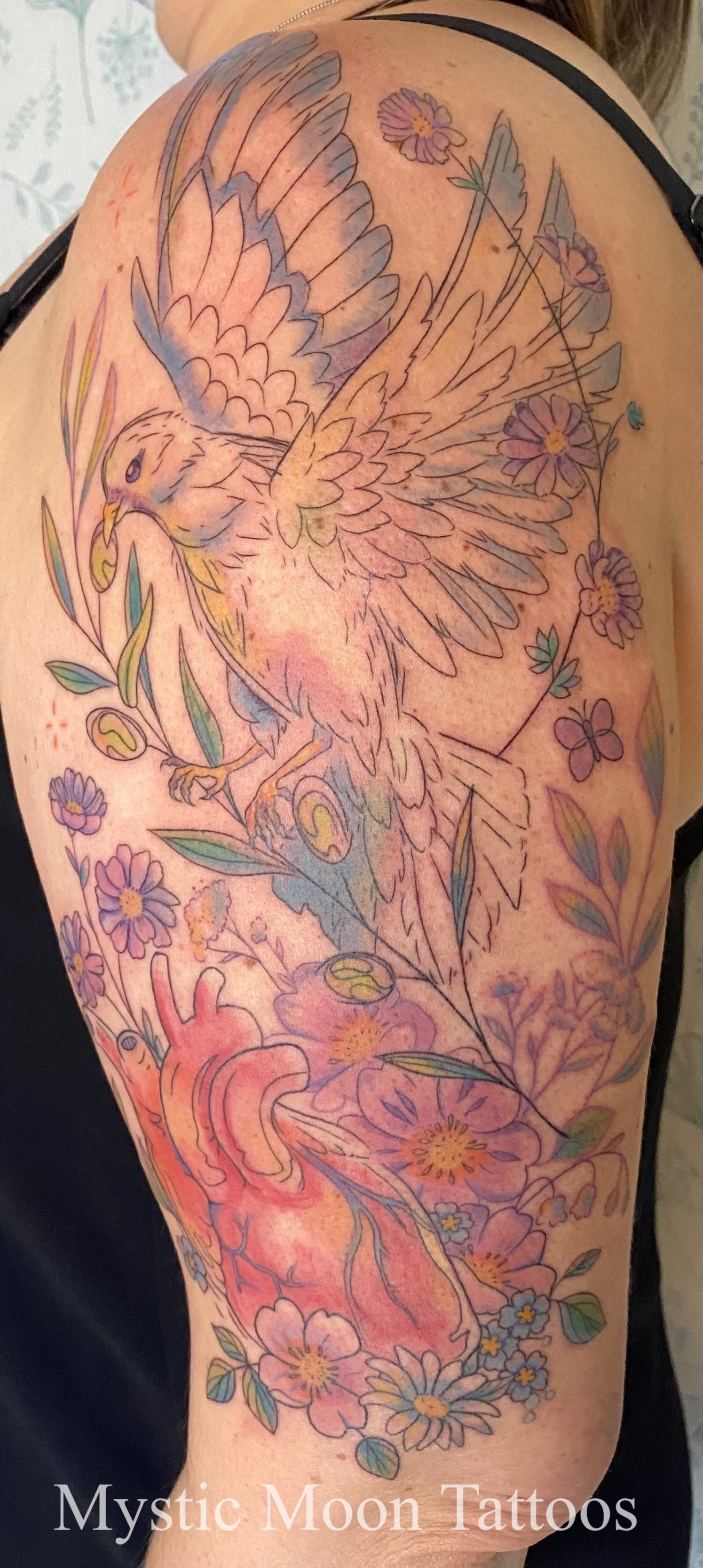 Delicate colour half sleeve, dove carrying olive branch over anatomical heart, surrounded by a plethora of mixed wild flowers.