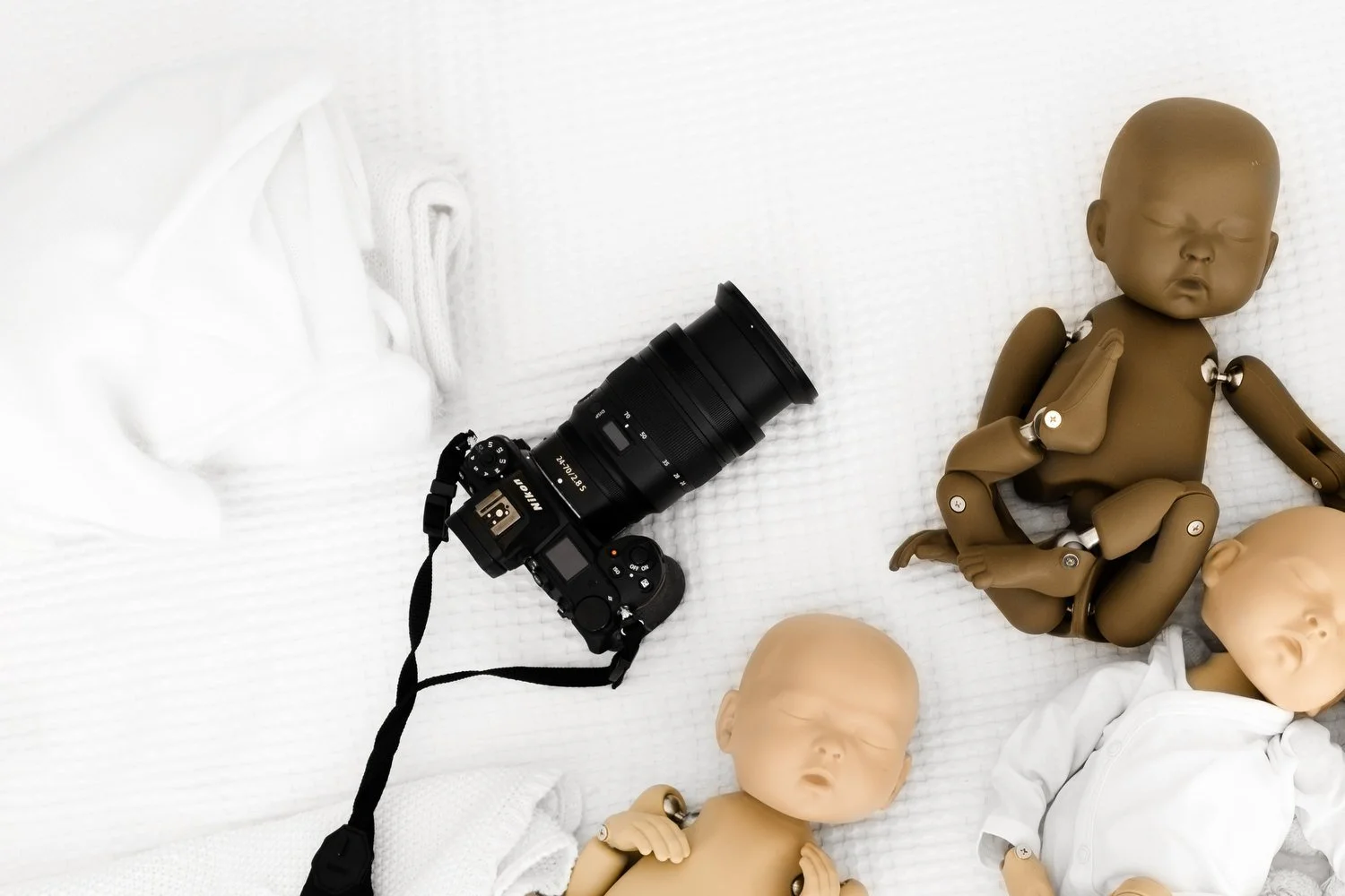Camera and zoom lens used for simple newborn photography setup on white bed with standinbabies