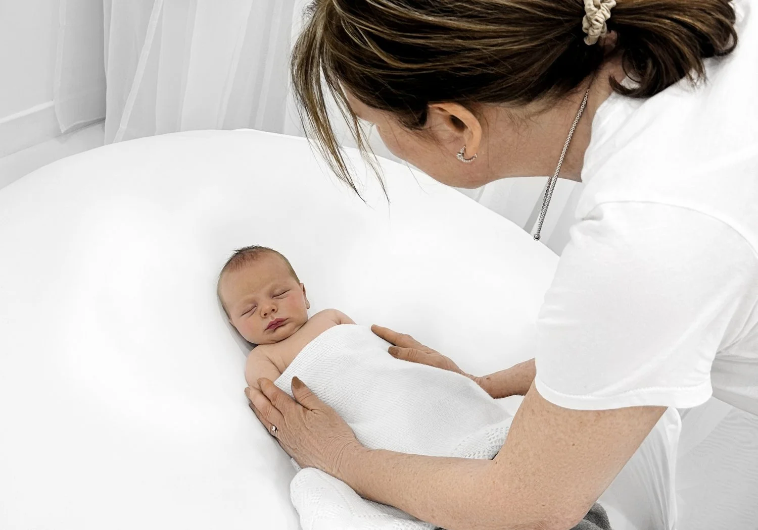 ally stuart ross gently positioning a newborn baby on a white beanbag in her minimalist studio