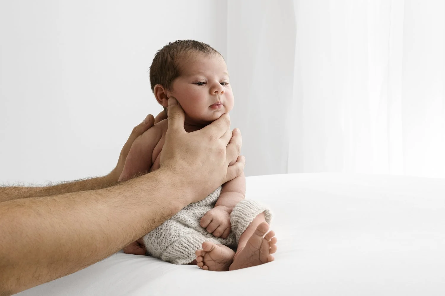 Dads hands holding newborn baby sitting in soft natural light