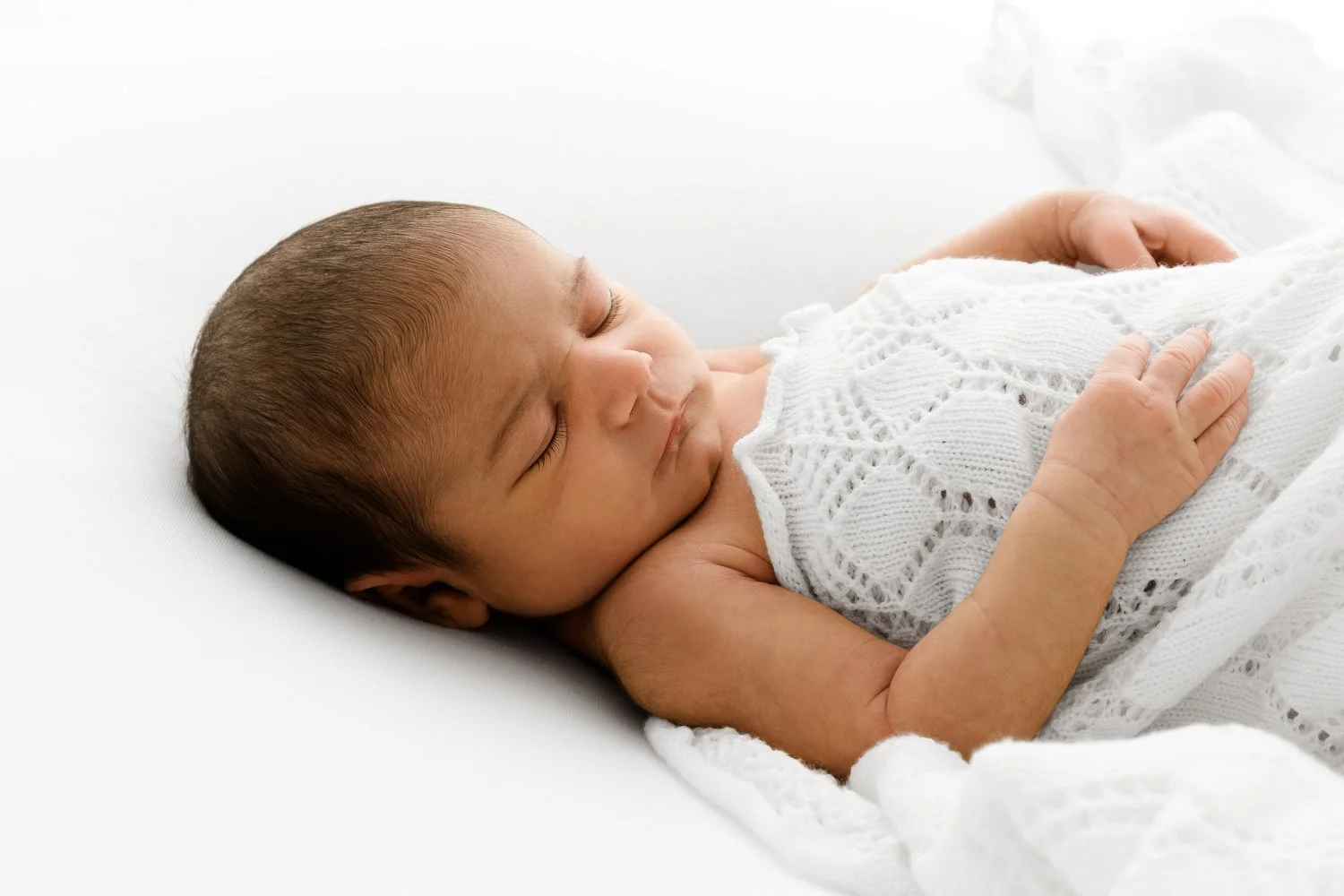 Minimal newborn photography example showing baby under white blanket with soft studio lighting