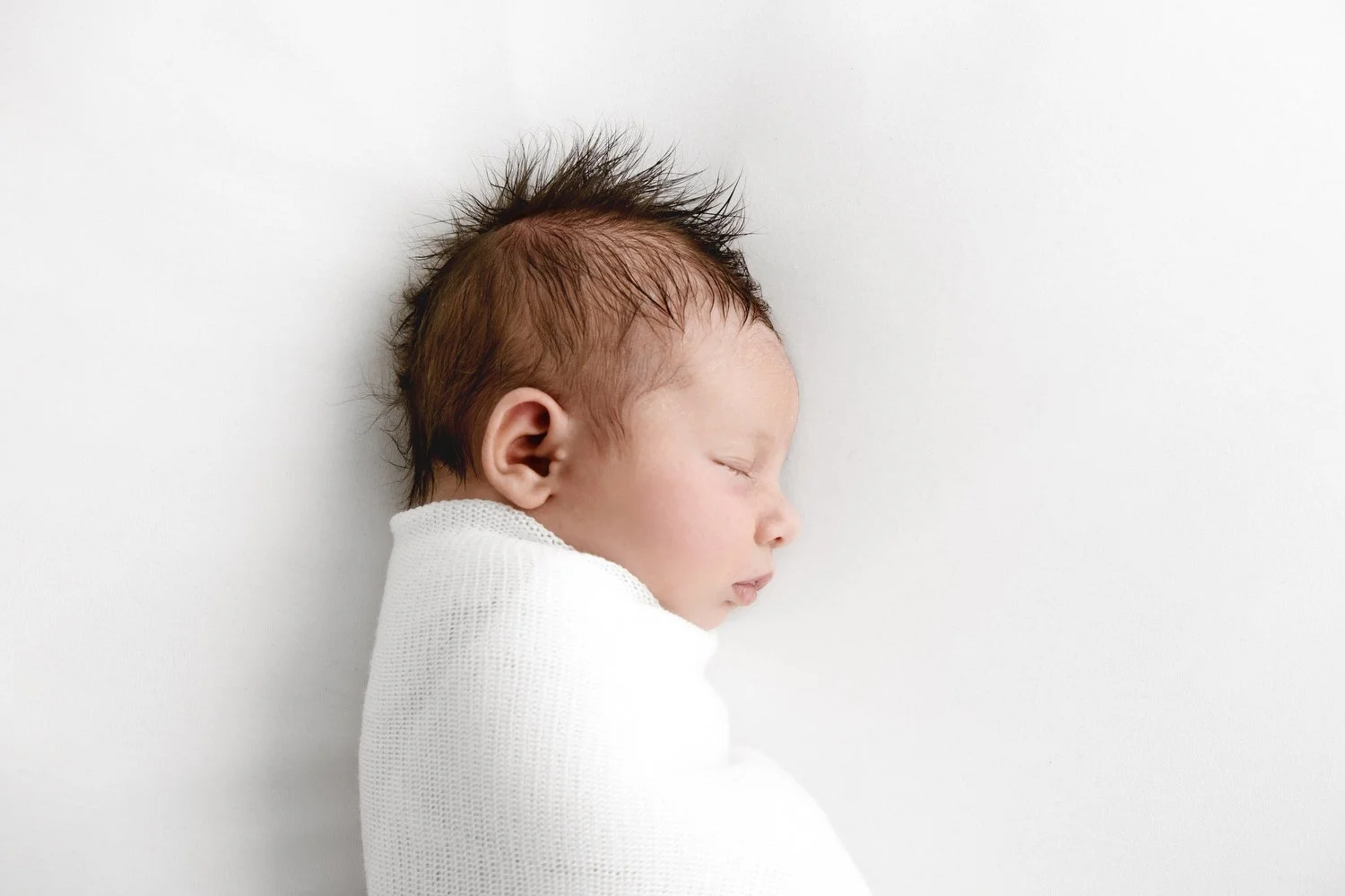 Sleeping newborn baby wrapped in white shawl at Mabel and Moose studio by Ally Stuart-Ross