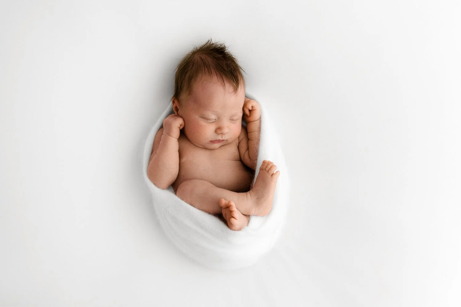 newborn baby wrapped in white natural wrap for a photography training session in united kingdom