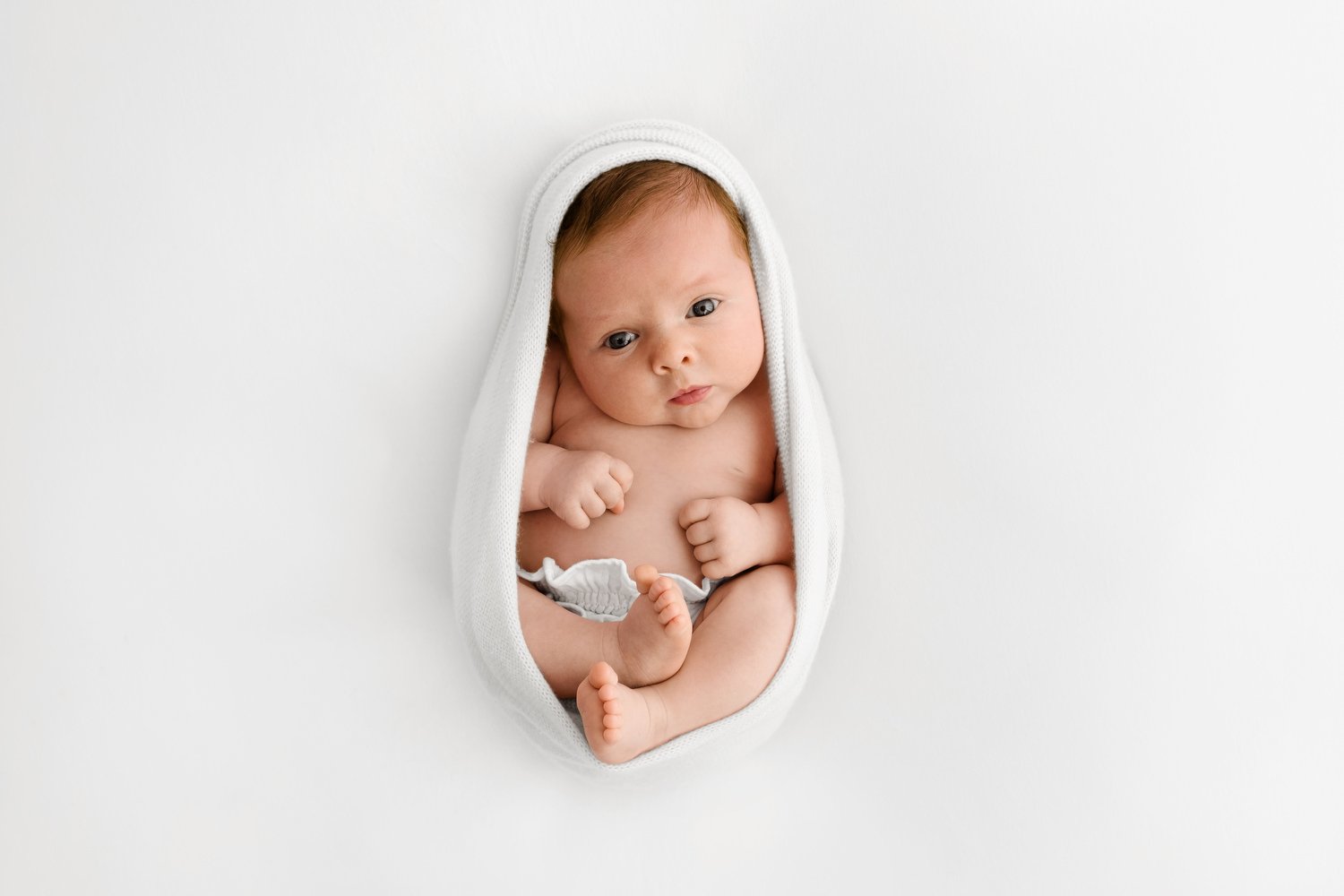 Wide awake newborn baby in a perfect cocoon wrap photographed in soft natural light demonstrating the calm skilled technique taught in Fokus online newborn photography mentoring by Mabel and Moose Education