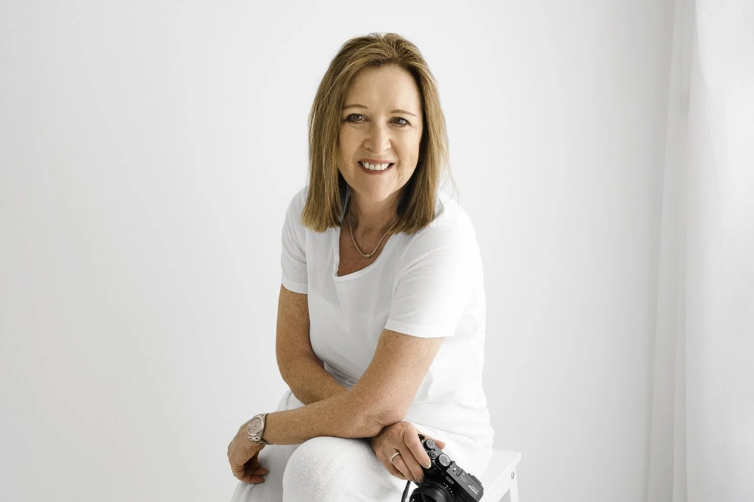 Newborn photography educator Ally Stuart-Ross holding her camera against a white background