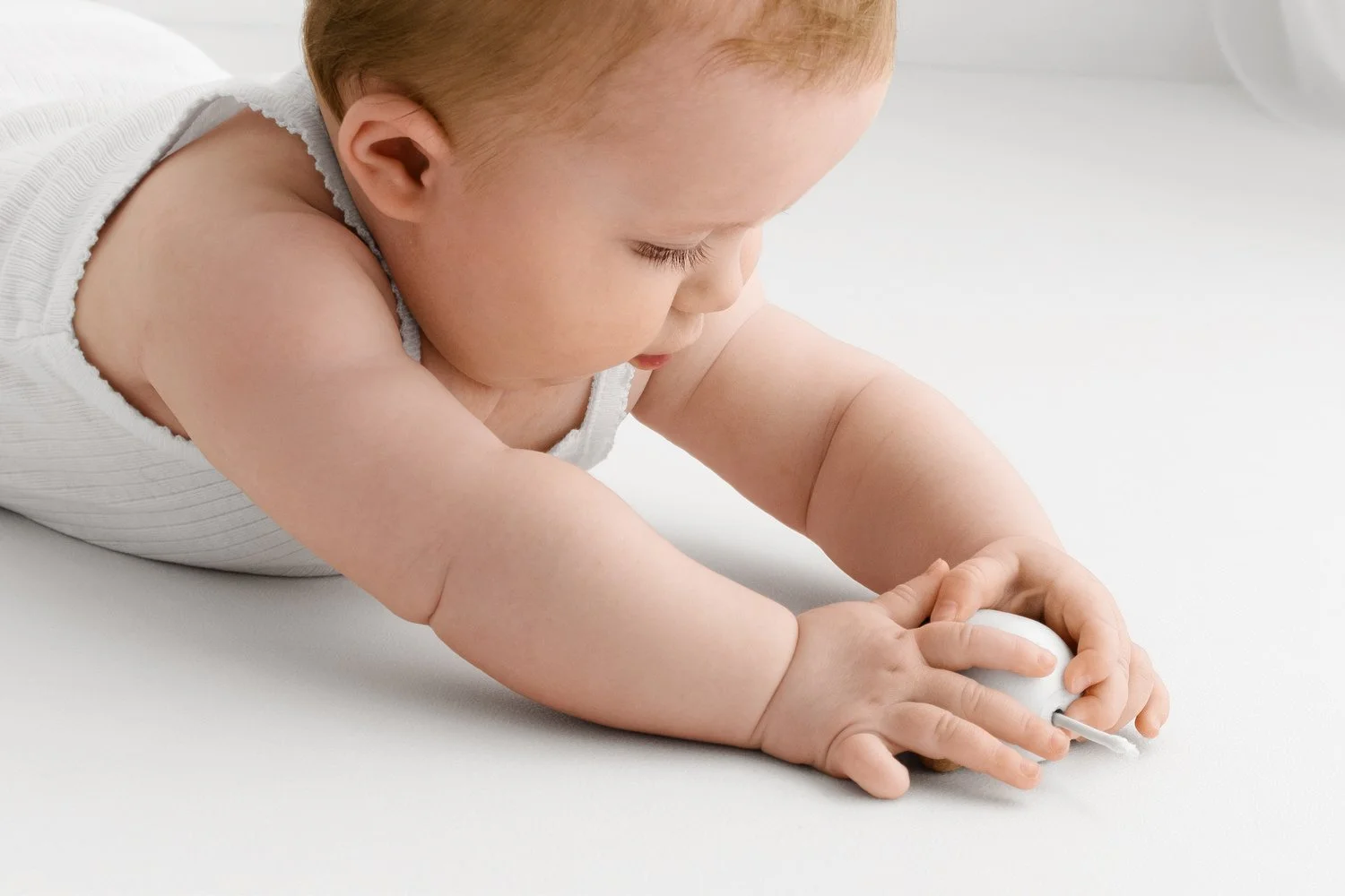 older baby on her tummy playing with a wooden toy shot using consistent aperture