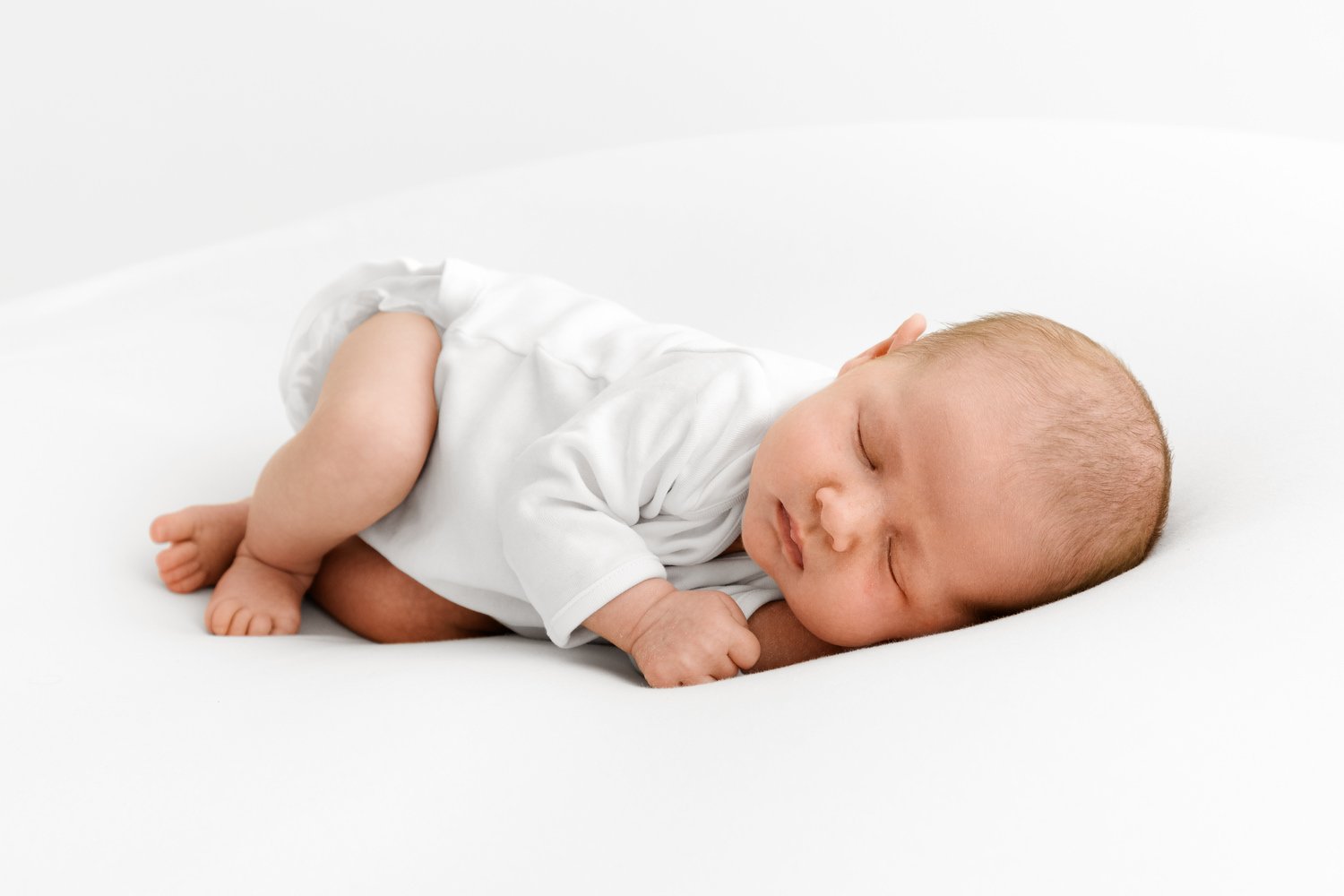Newborn baby lying on side in white at Mabel and Moose studio by Ally Stuart-Ross