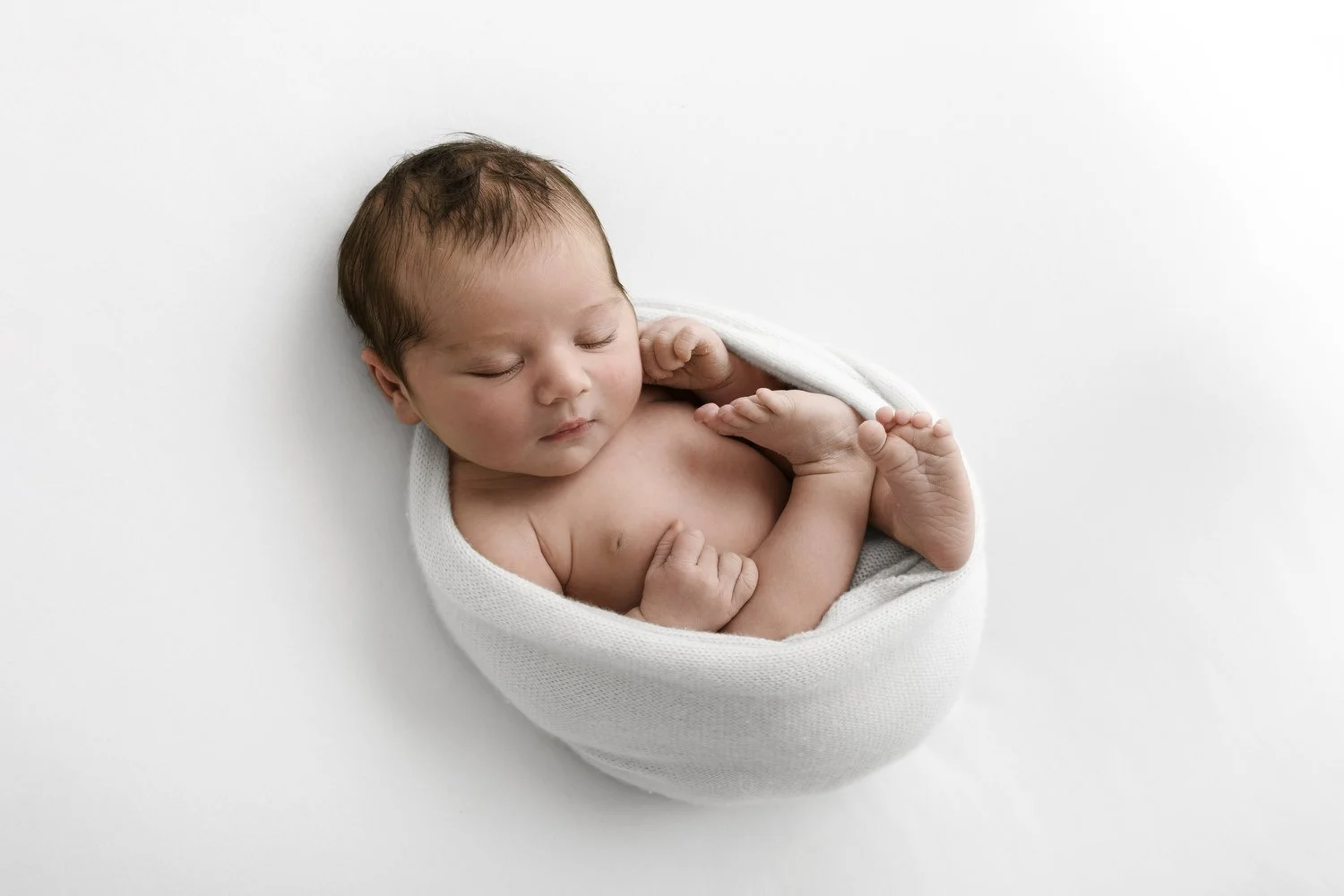 sleeping newborn baby in a beautiful white cocoon womb wrap demonstrating the calm minimal wrapping style taught in the Mabel and Moose Method