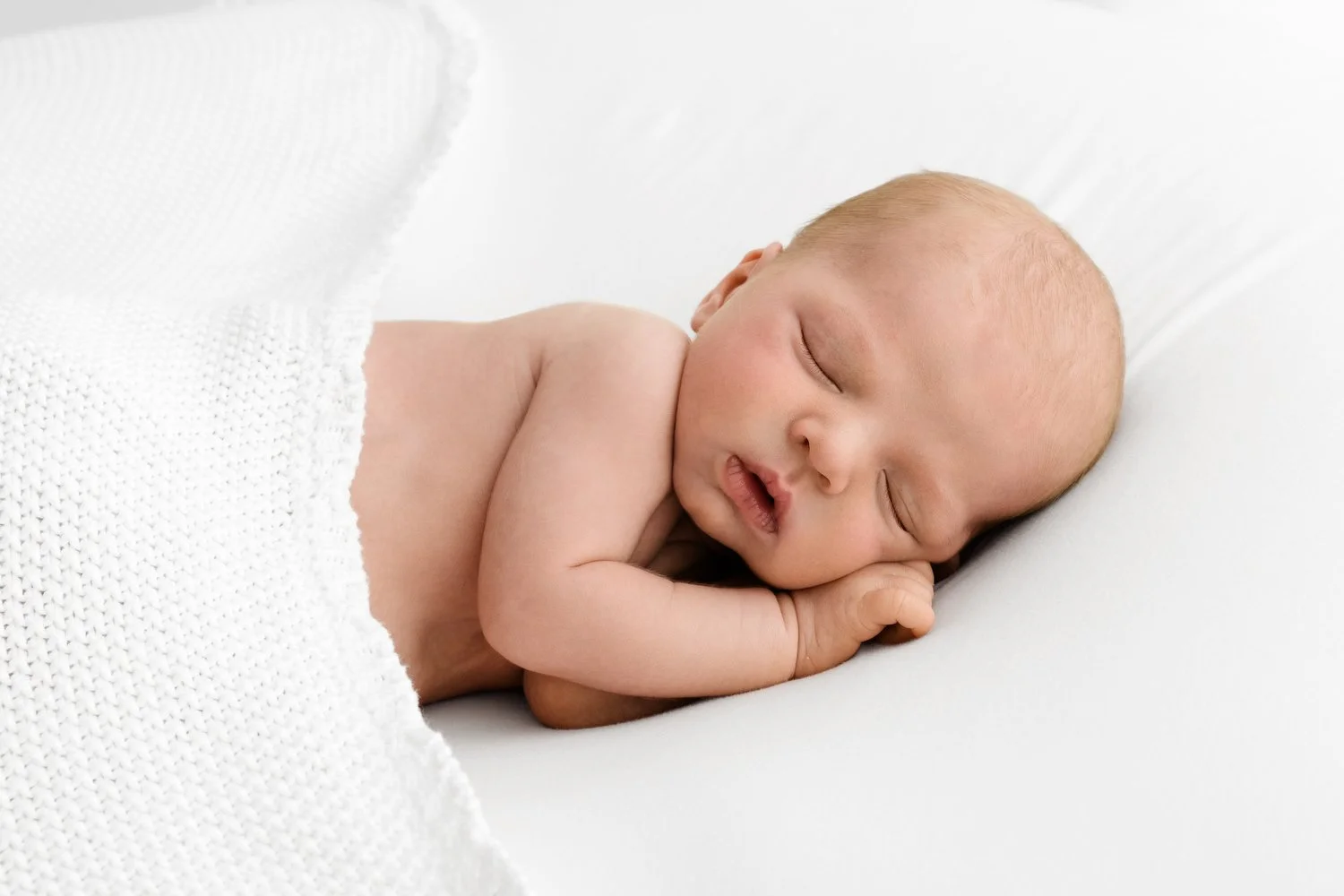 newborn baby lying on side under white blanket lifestyle newborn photography