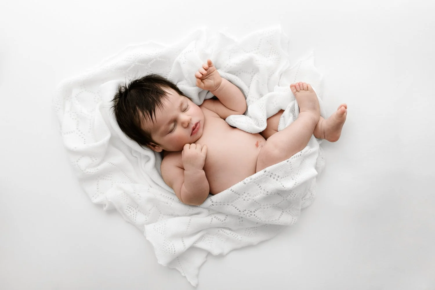 Overhead shot of sleeping newborn baby in relaxed natural pose on white lace shawl lifestyle newborn photography