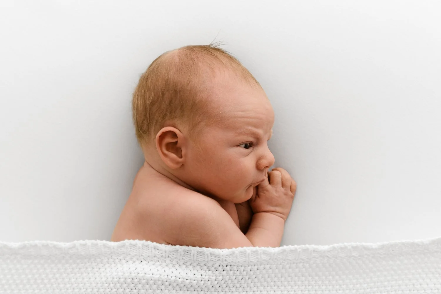 Awake newborn baby lying on side under white blanket lifestyle newborn photography