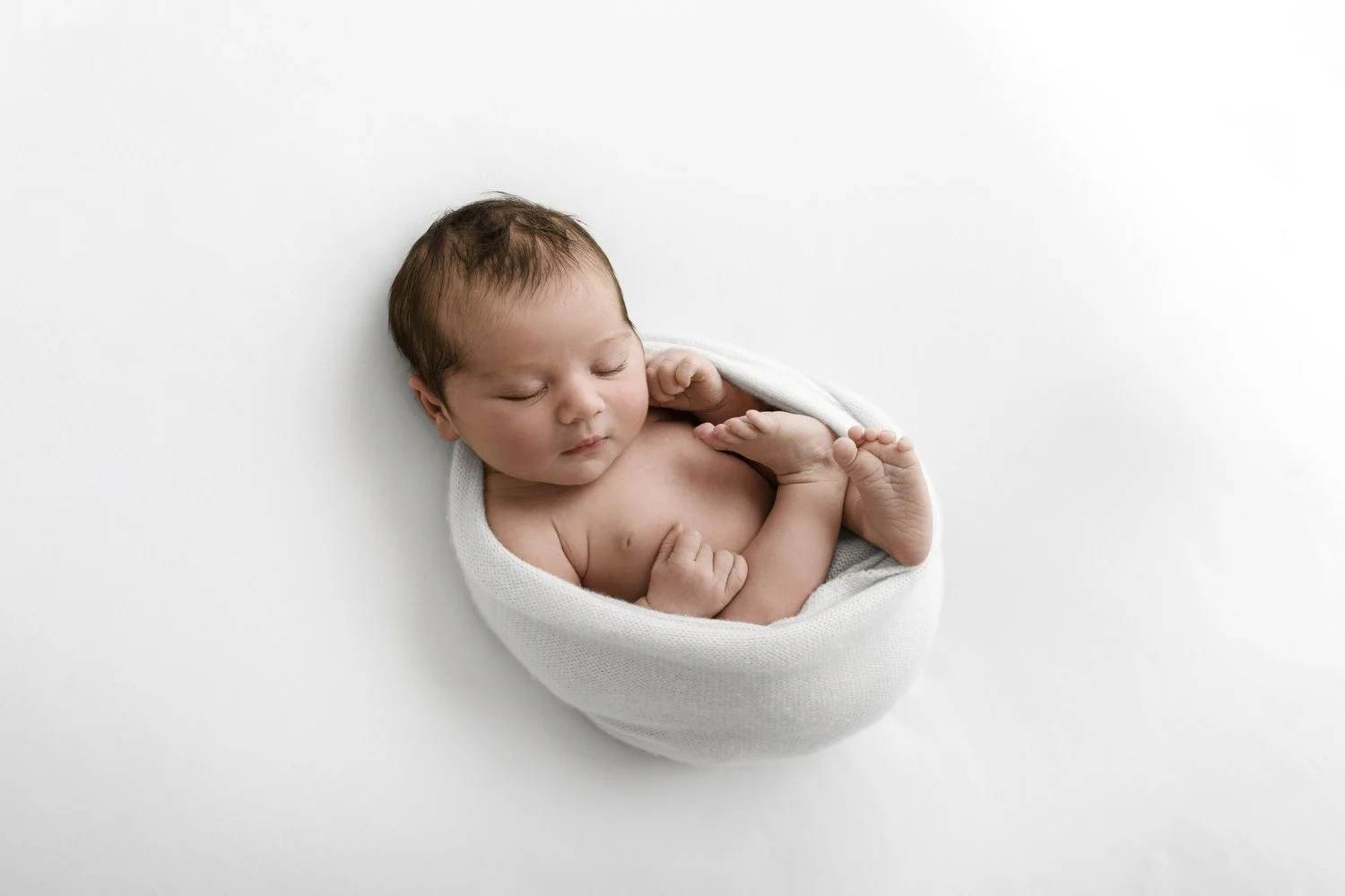 Curled newborn baby wrapped in white lifestyle newborn photography