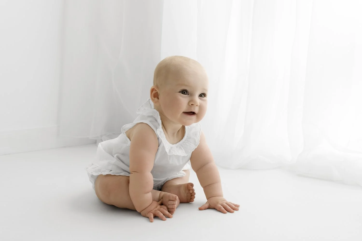 Older baby sitting independently in soft natural light against a white backdrop in a minimalist studio