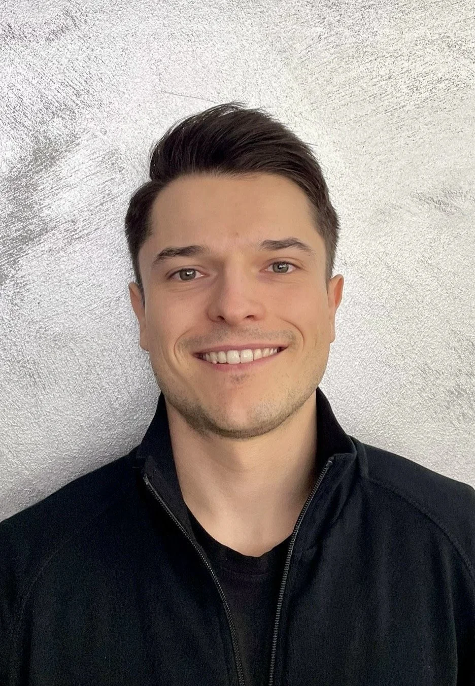 Portrait eines lächelnden Mannes vor einem grauen Hintergrund.