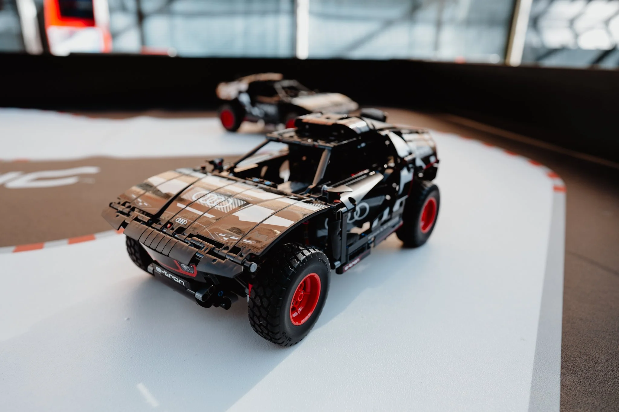 Ein LEGO-Modell eines schwarzen Audi Quattro mit roten Felgen auf einer weißen Oberfläche, vermutlich auf einem Miniatur-Rennstrecke.