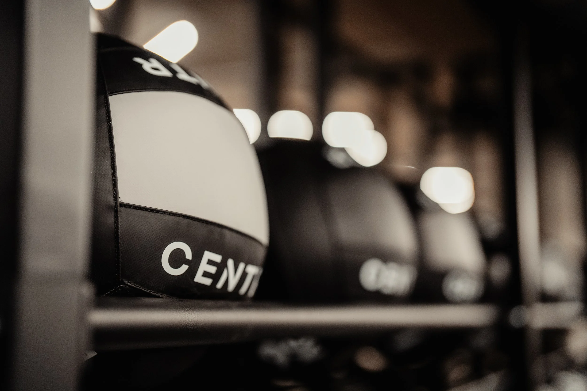 Gepolsterte Kettlebell mit der Aufschrift 'CENTR' auf einer Halle mit weiteren Kettlebells im Hintergrund, unscharf.
