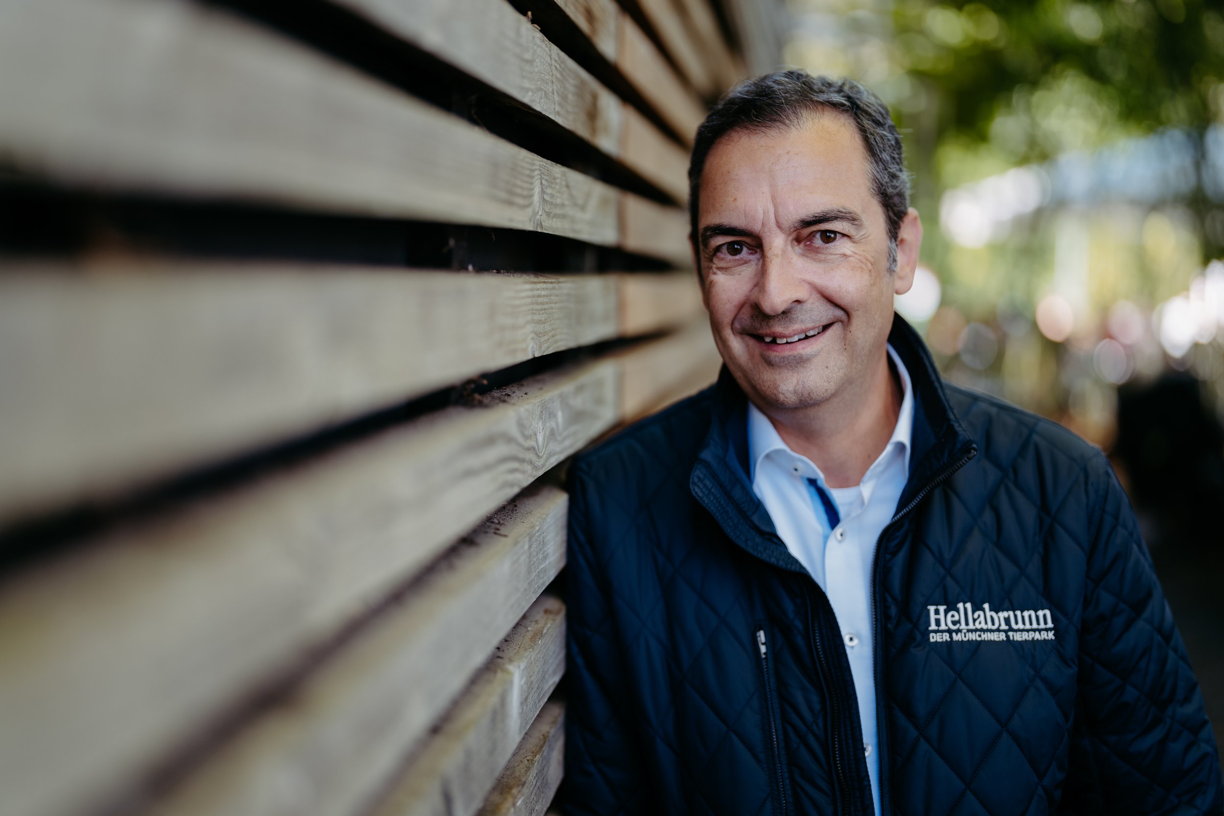 Mann mit dunkelblauer Jacke vor Holzwand