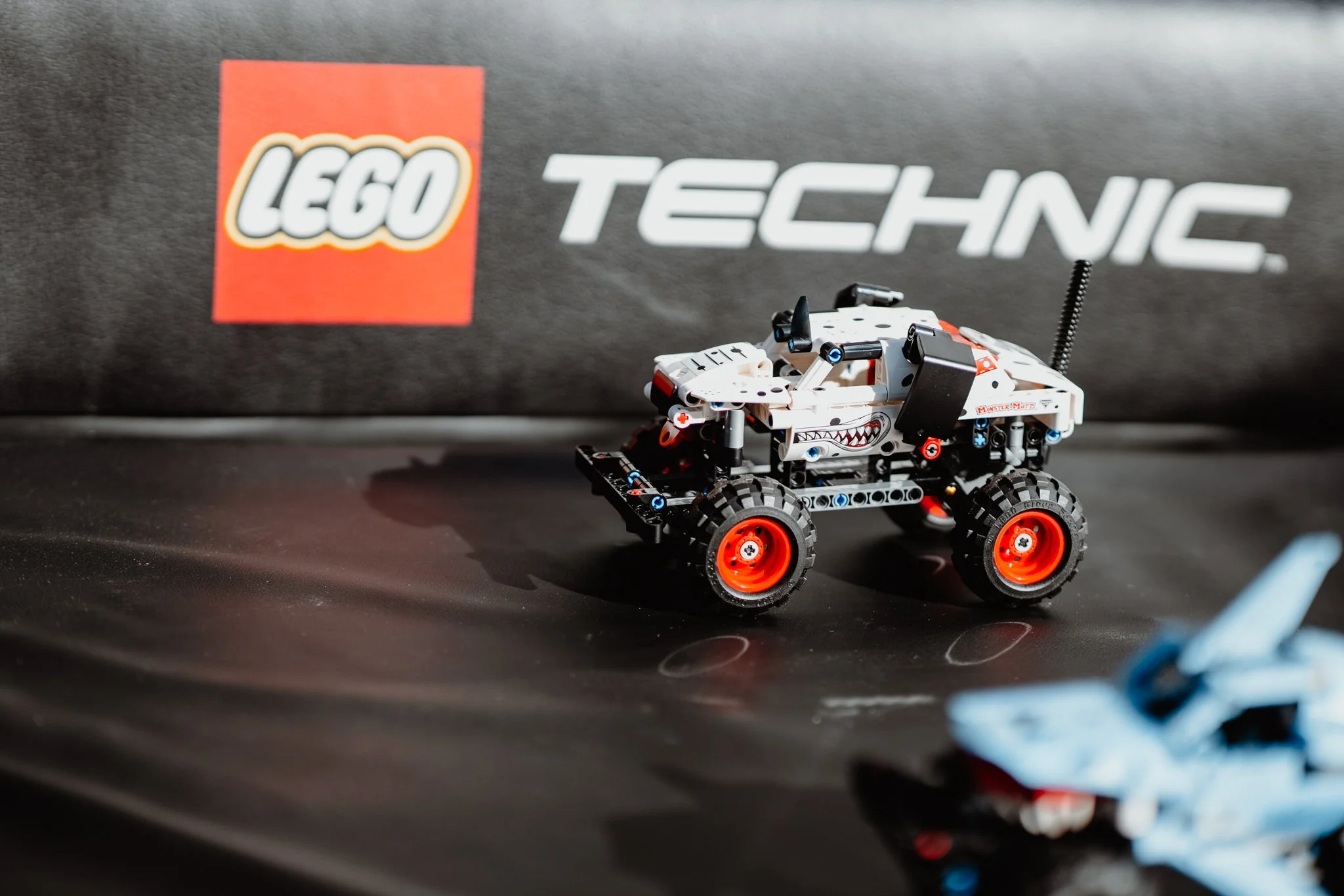 Ein LEGO Technic Roboter im Nahaufnahme, mit roten Rädern und einem weißen Körper, auf einem schwarzen Untergrund, im Hintergrund ein LEGO Logo und die Marke "TECHNIC".