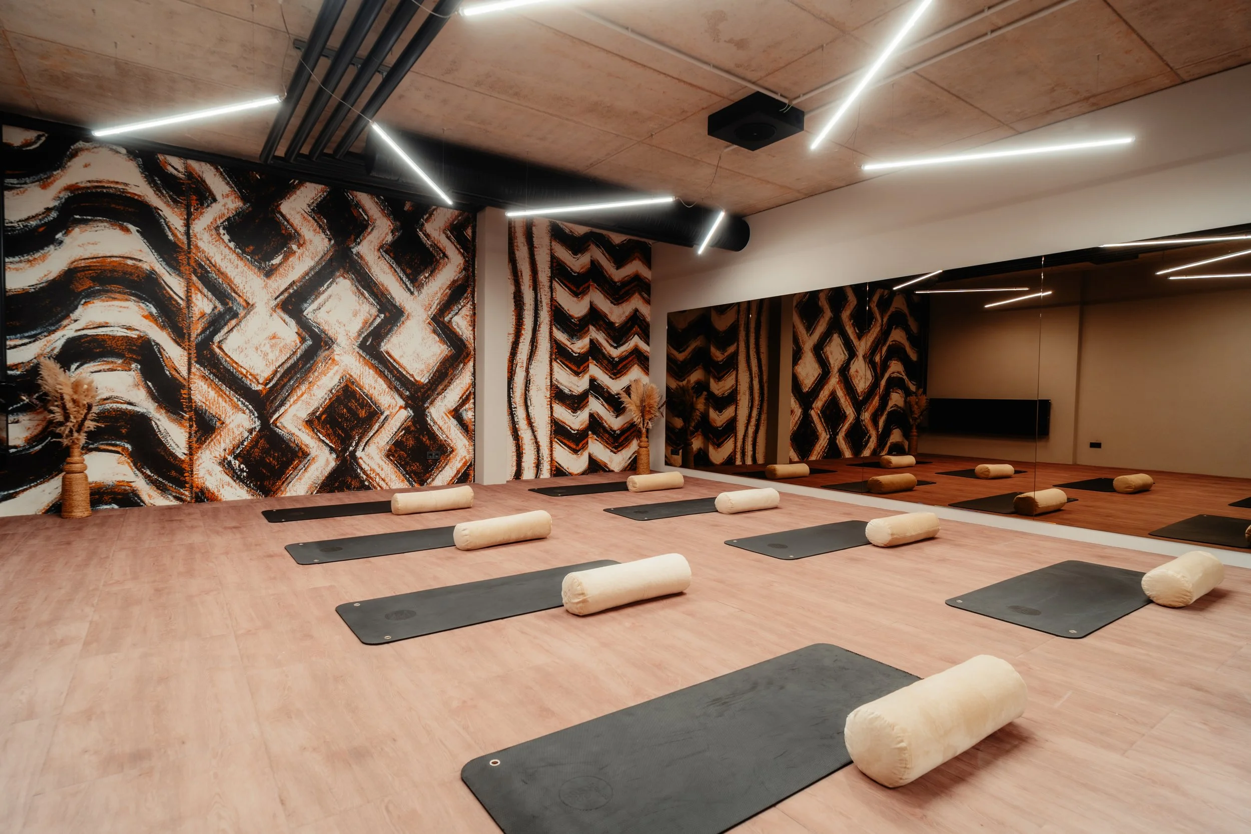 Innenraum eines Yoga-Studios mit schwarzen Yoga-Matten, Bolster, Wandbilder mit afrikanischen Mustern und Spiegelwänden.