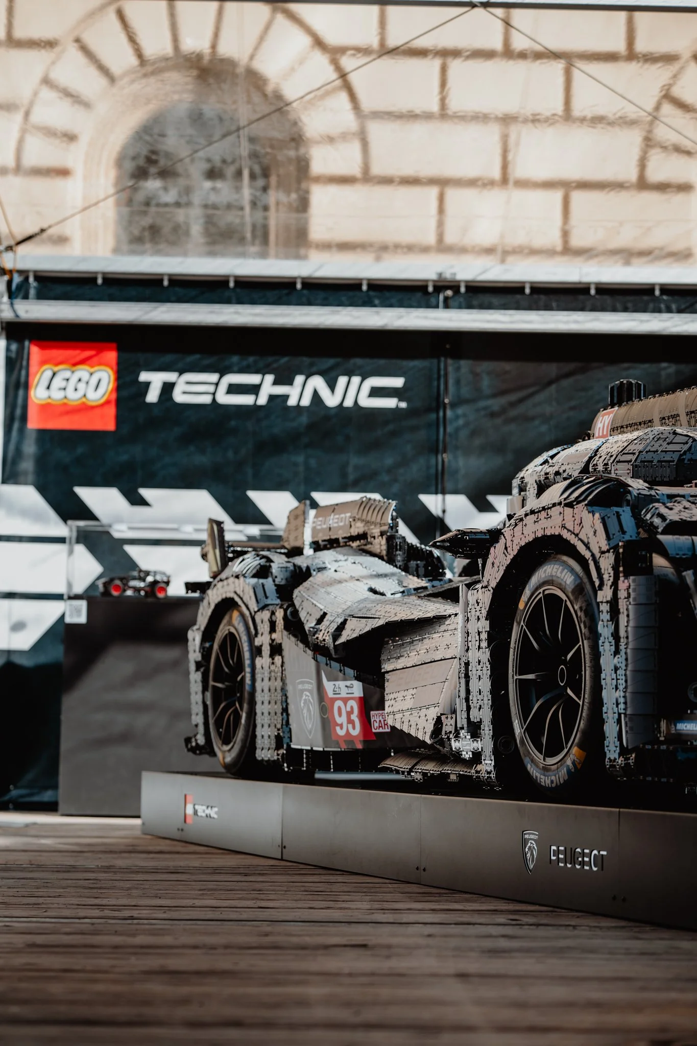 Ein LEGO-Modell eines Rennwagens auf einer Ausstellungstafel, mit einem LEGO TECHNIC-Logo im Hintergrund.