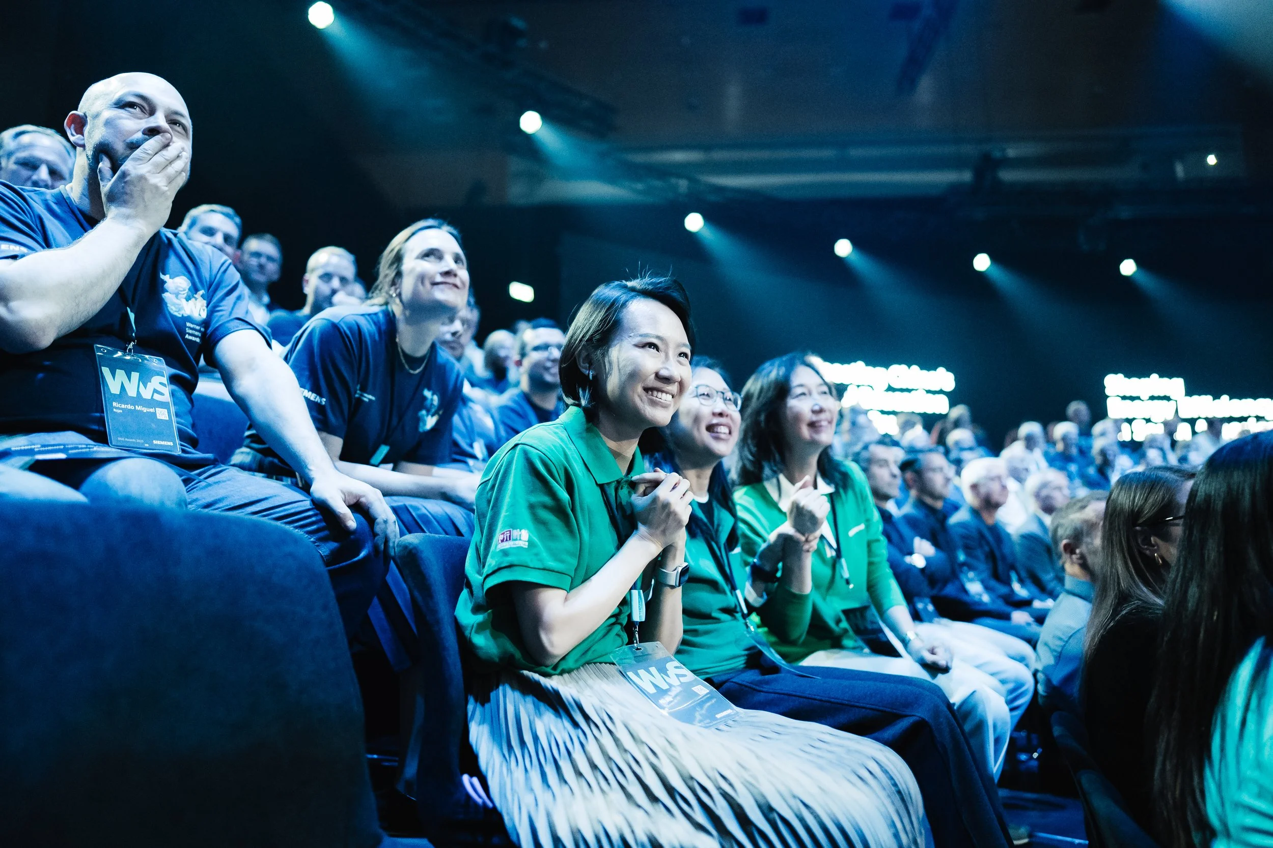 Menschen bei einer Konferenz, lachend und begeistert, im dunklen Raum mit blauem Licht, einige tragen Namensschilder mit dem Logo 'WSE'.