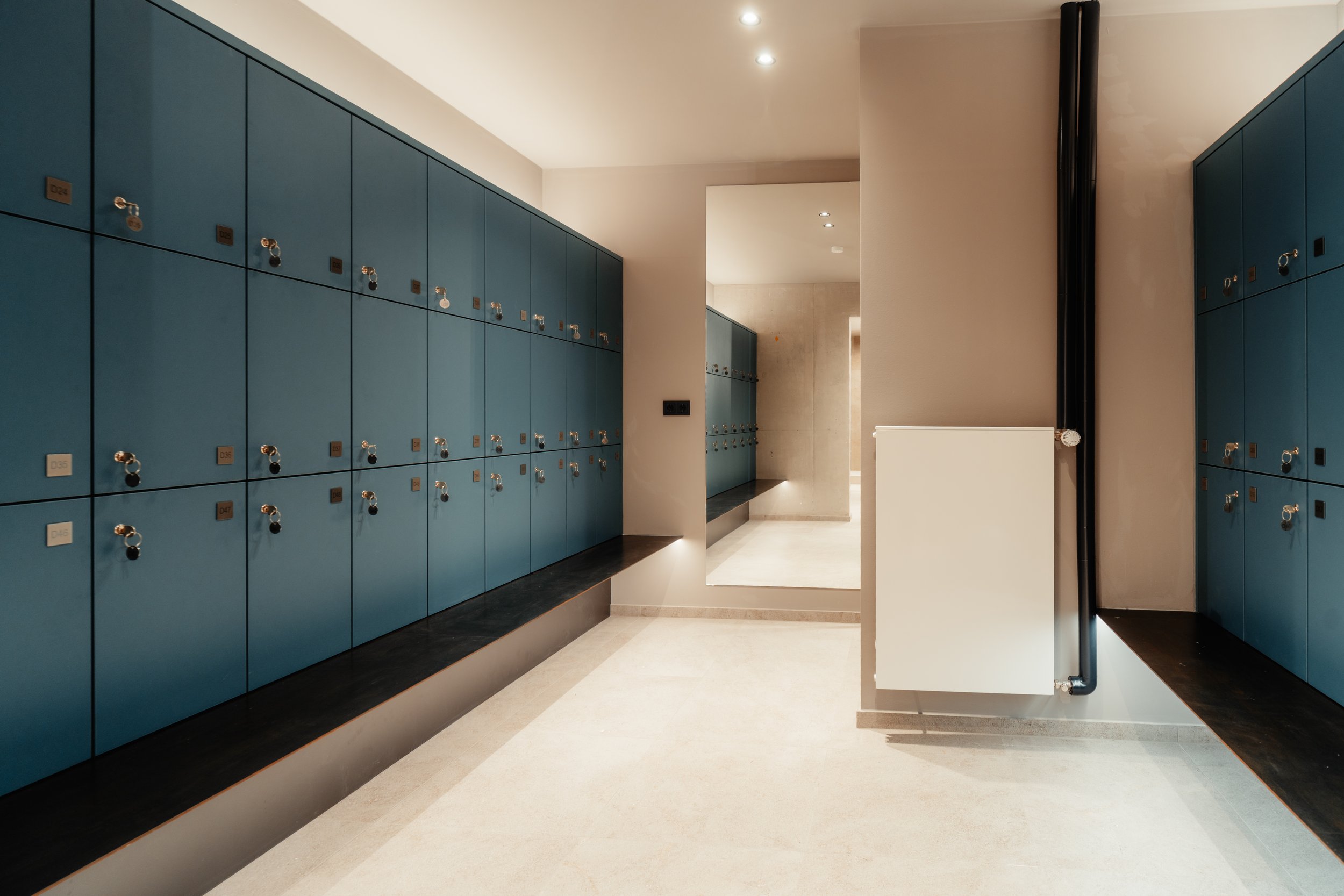 Blaue Spinde in einem Fitnessstudio oder Schwimmbad, mit einem schmalen Spiegel in der Mitte und Heizkörper rechts daneben.