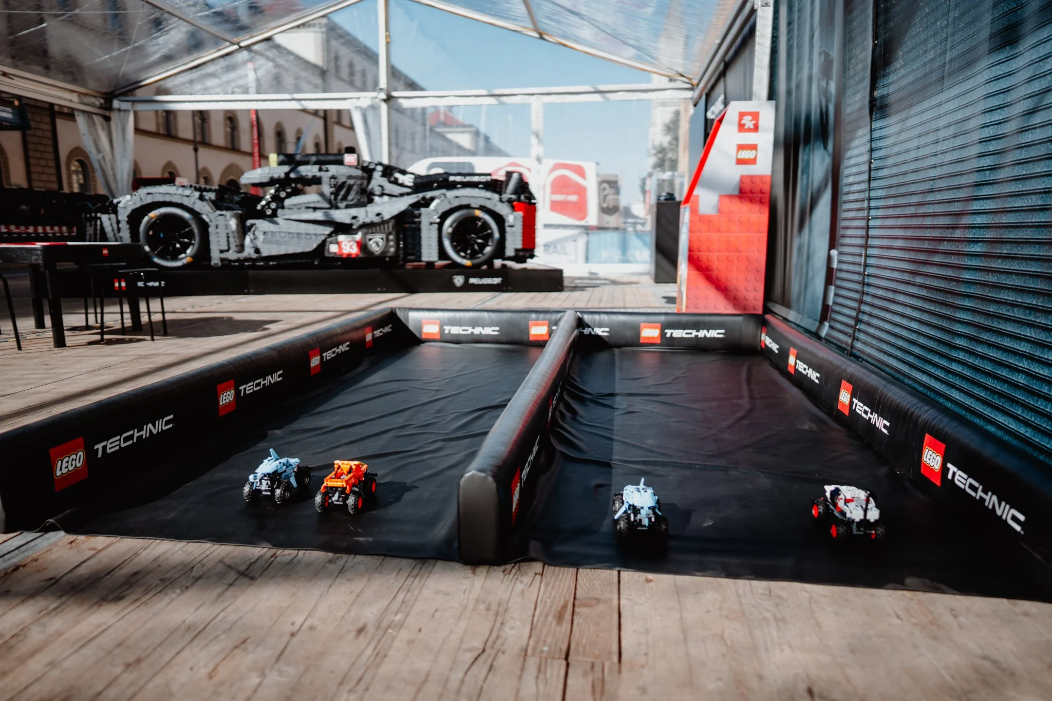 Lego Technic Miniaturmodell eines Rennwagens auf einer Lego-Track, im Hintergrund ein größeres Lego-Model eines Rennwagens.