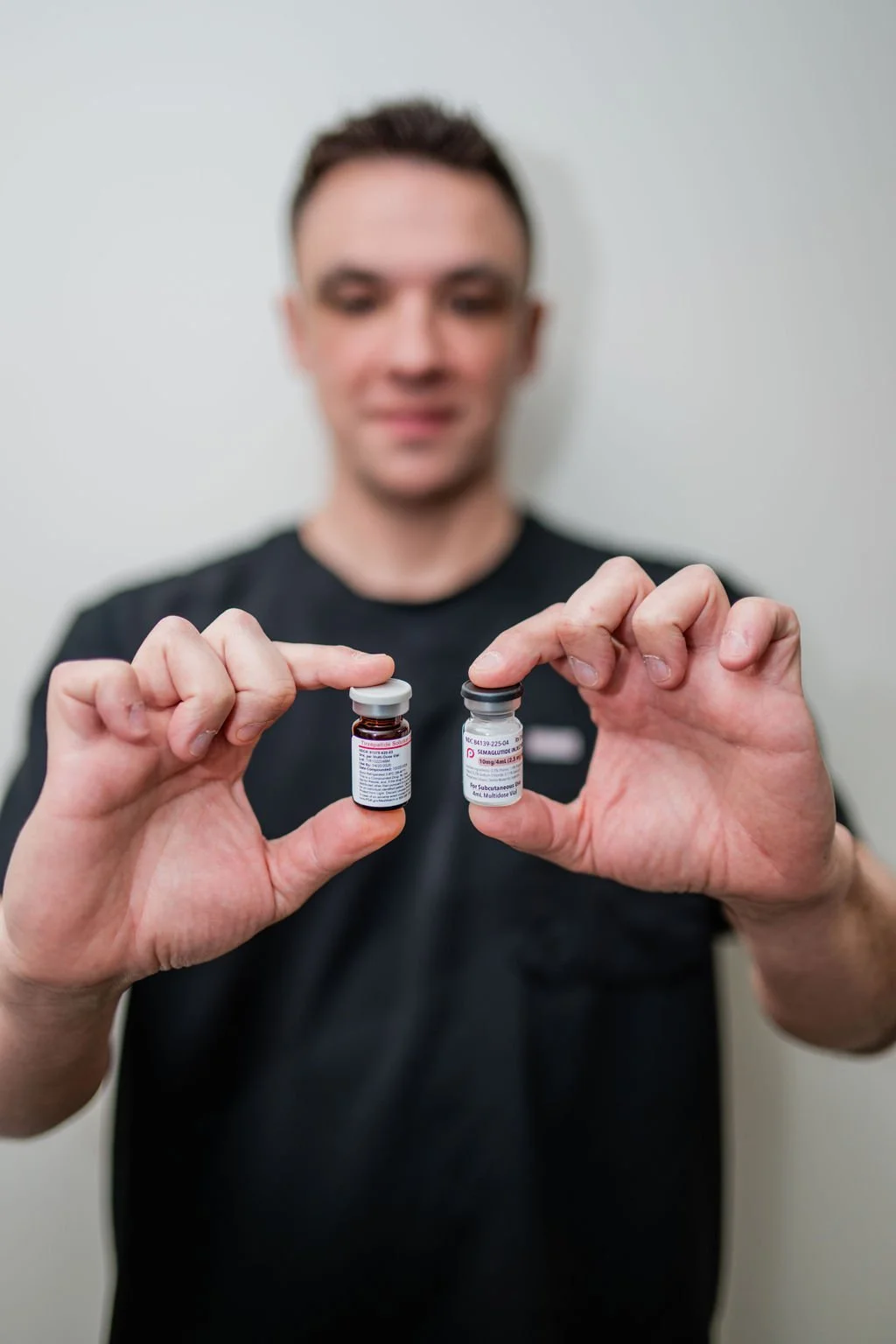 A man holding two vials of medication, one in each hand, with the labels visible.