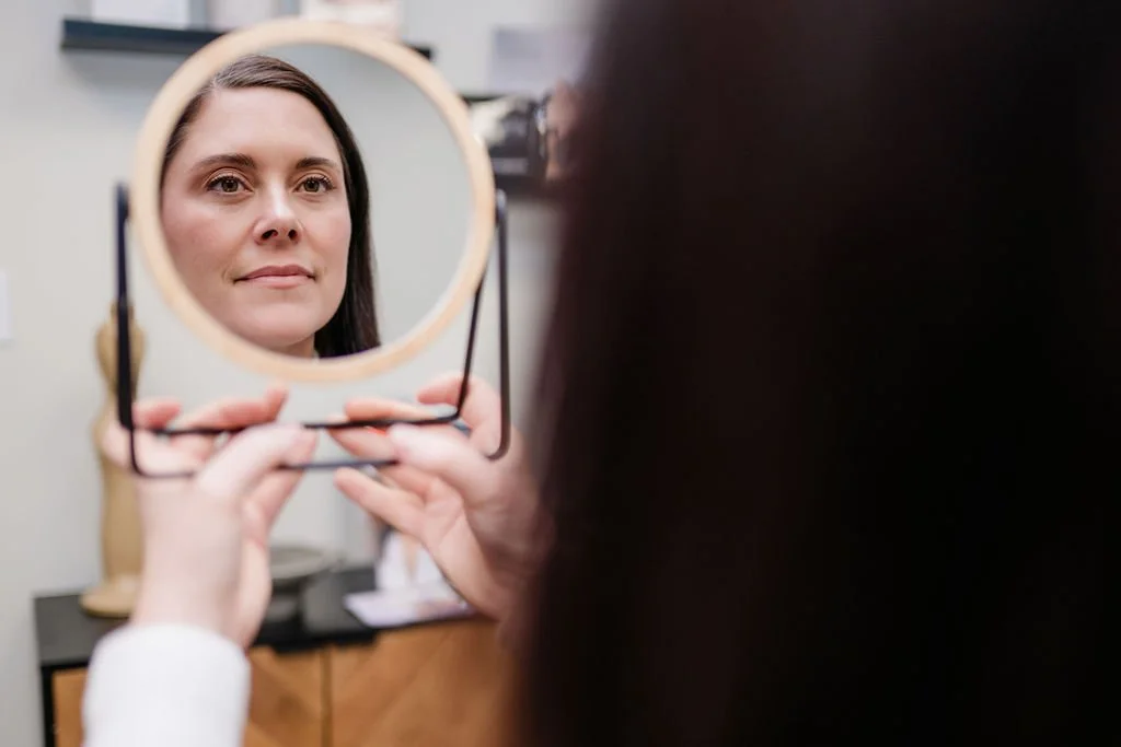 Woman looking into a mirror while holding the mirror in her hands.