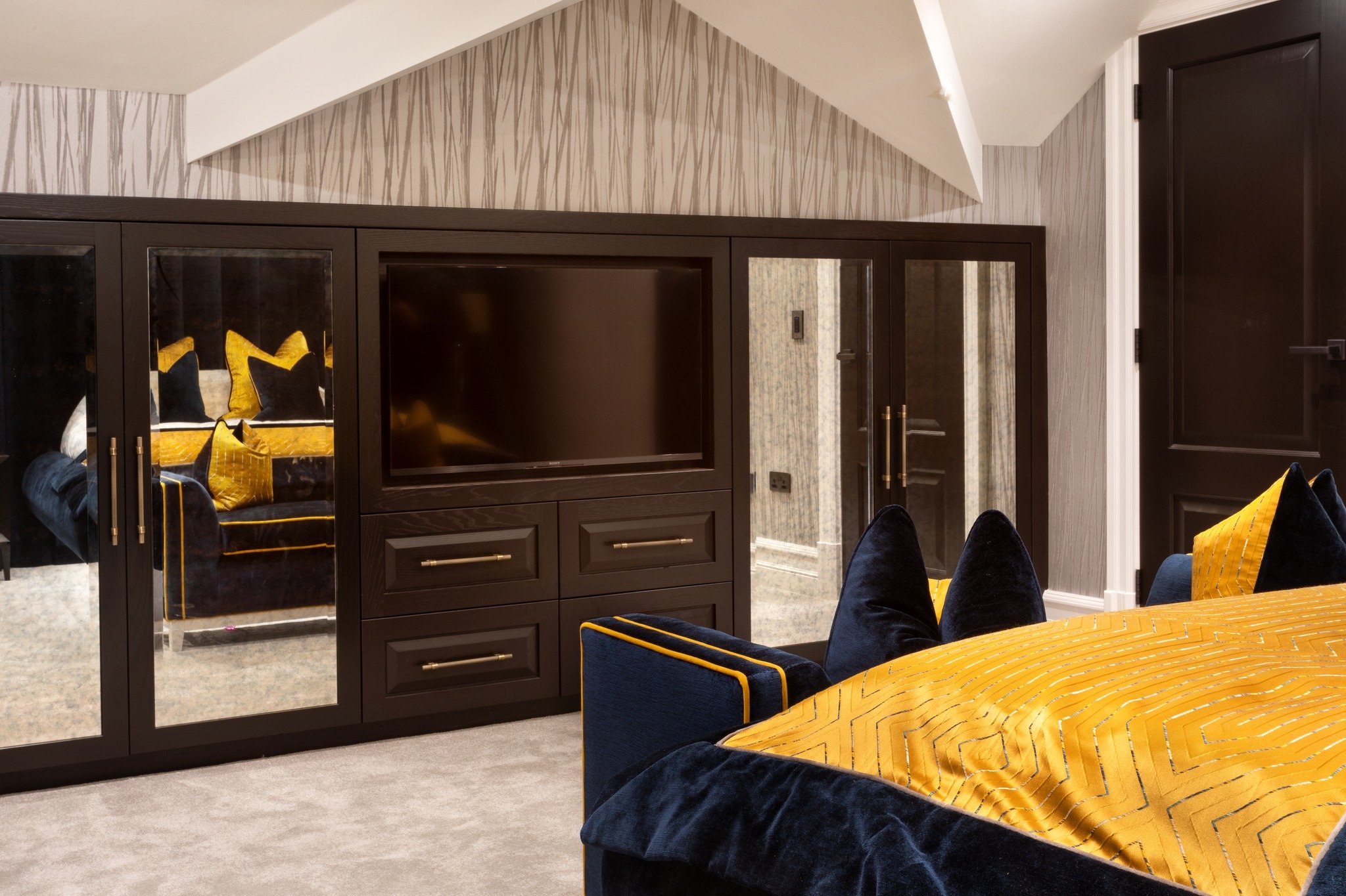 Proof that sloped ceilings don't mean sacrificing style. This custom media wall is a masterclass in multifunctional storage. A smart TV unit framed perfectly by bespoke dark wood cabinetry in wenge. Seamlessly built into the eaves to maximize storage