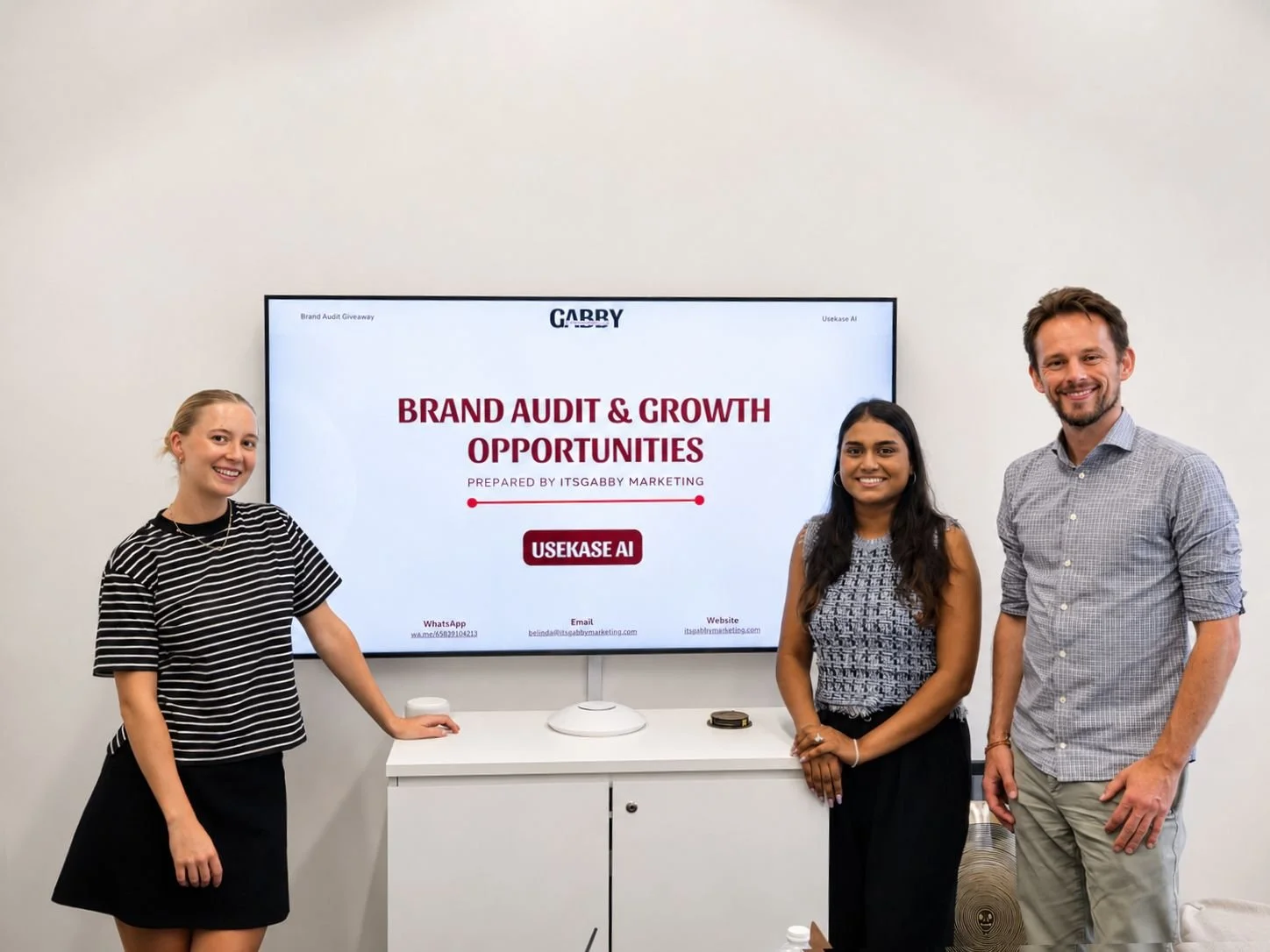 Founder of ItsGabby Marketing company with Founder of an AI company. Three people standing in front of a large screen displaying a presentation titled 'Brand Audit & Growth Opportunities'.