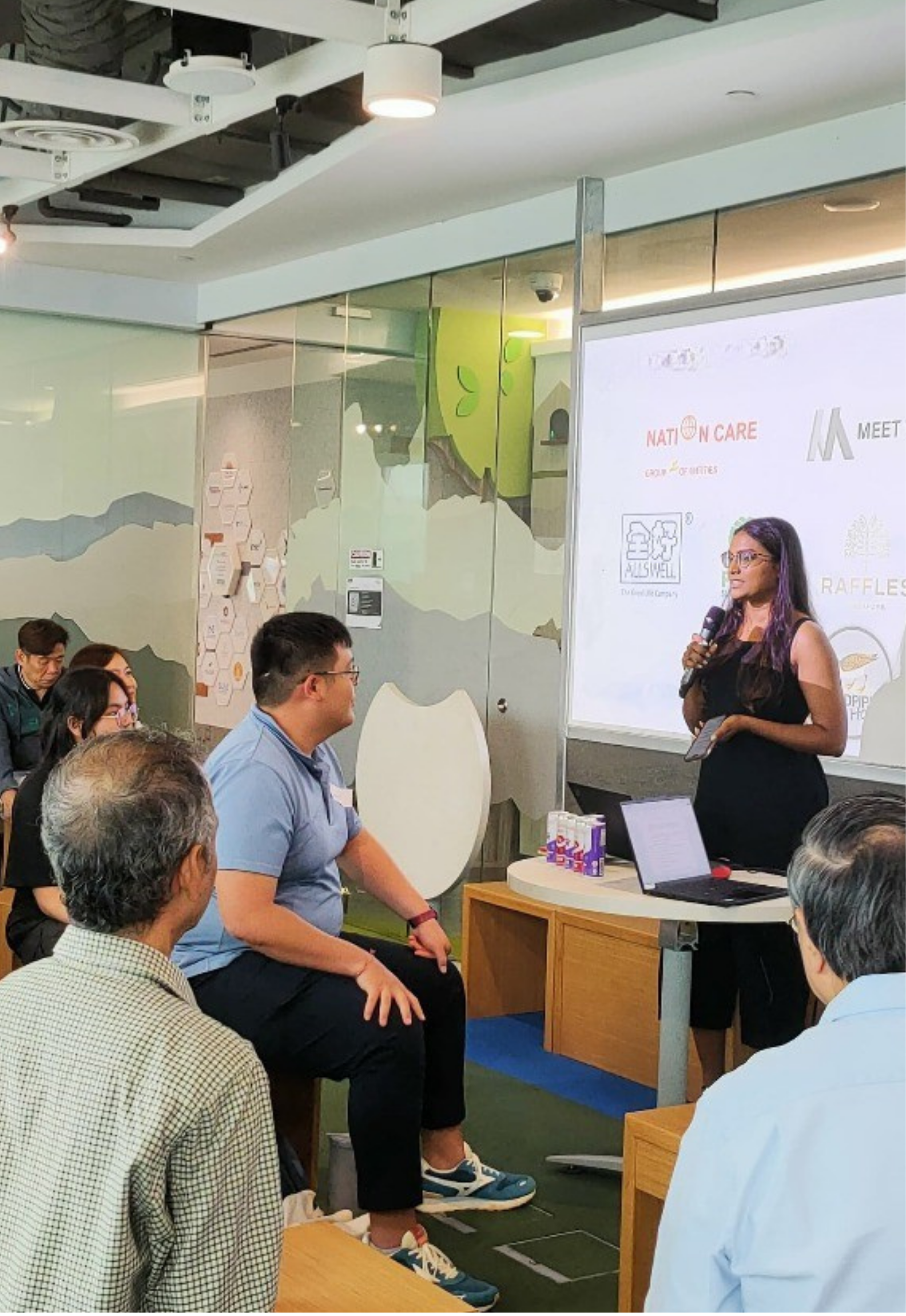 Founder of ItsGabby Marketing company giving a presentation to a group of people seated in a room with a large screen. The room has modern decor with wall art and ceiling lights, and the audience appears attentive.