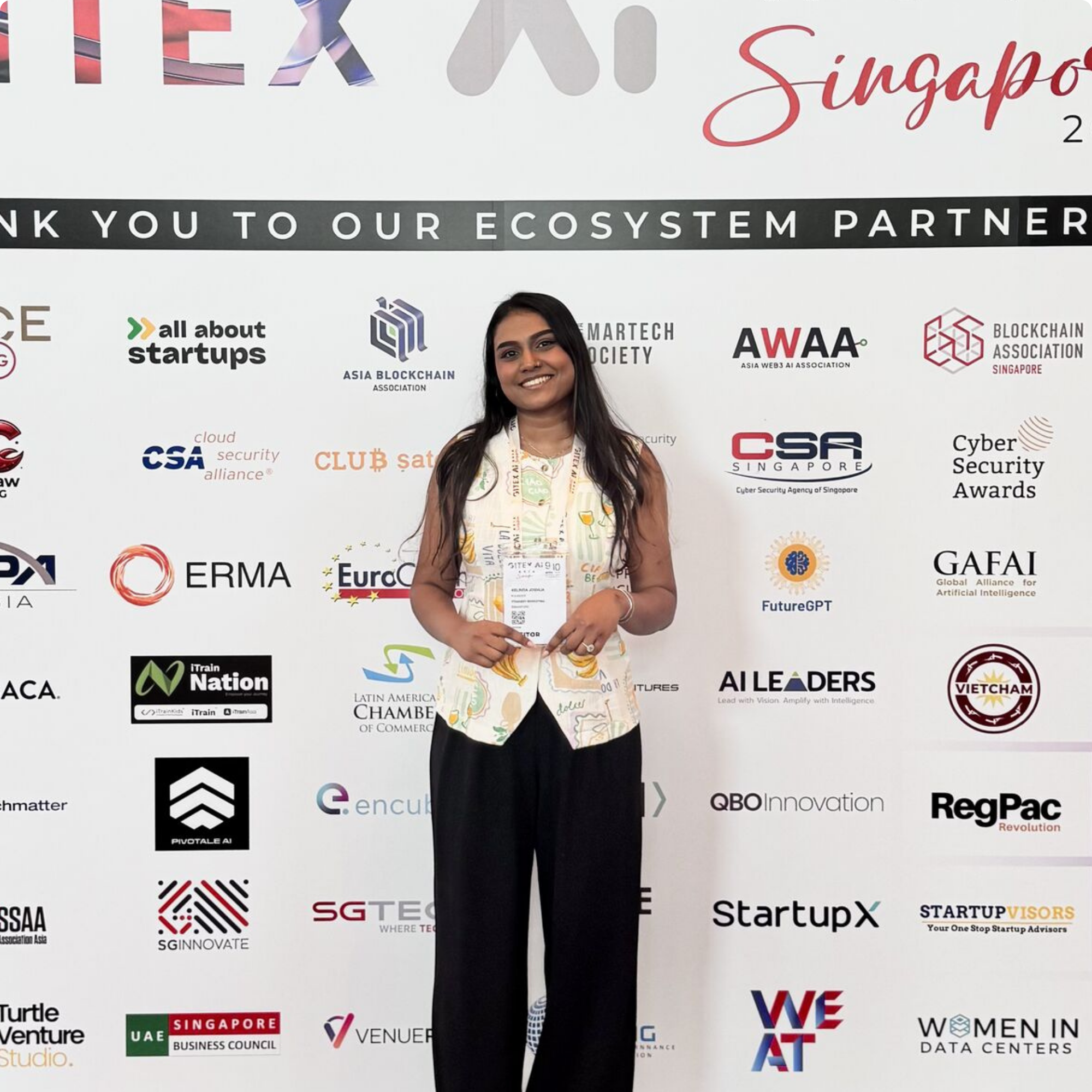 Founder of ItsGabby Marketing company smiling at a conference with a backdrop displaying various technology company logos and the text 'Thank you to our ecosystem partners.'