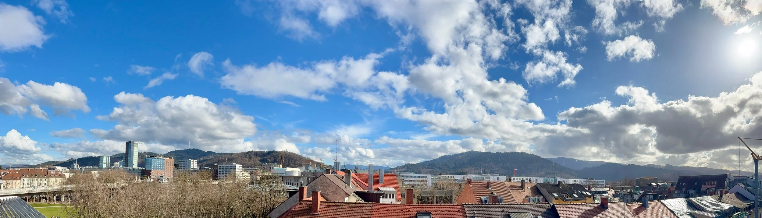 Panorama von Freiburg im Breisgau mit Wolken am Himmel und dem Schwarzwald im Hintergrund. Das Foto wurde aus den Räumen der Kanzlei Stolterfoth - Rechtsanwaltskanzlei für Strafrecht aufgenommen.